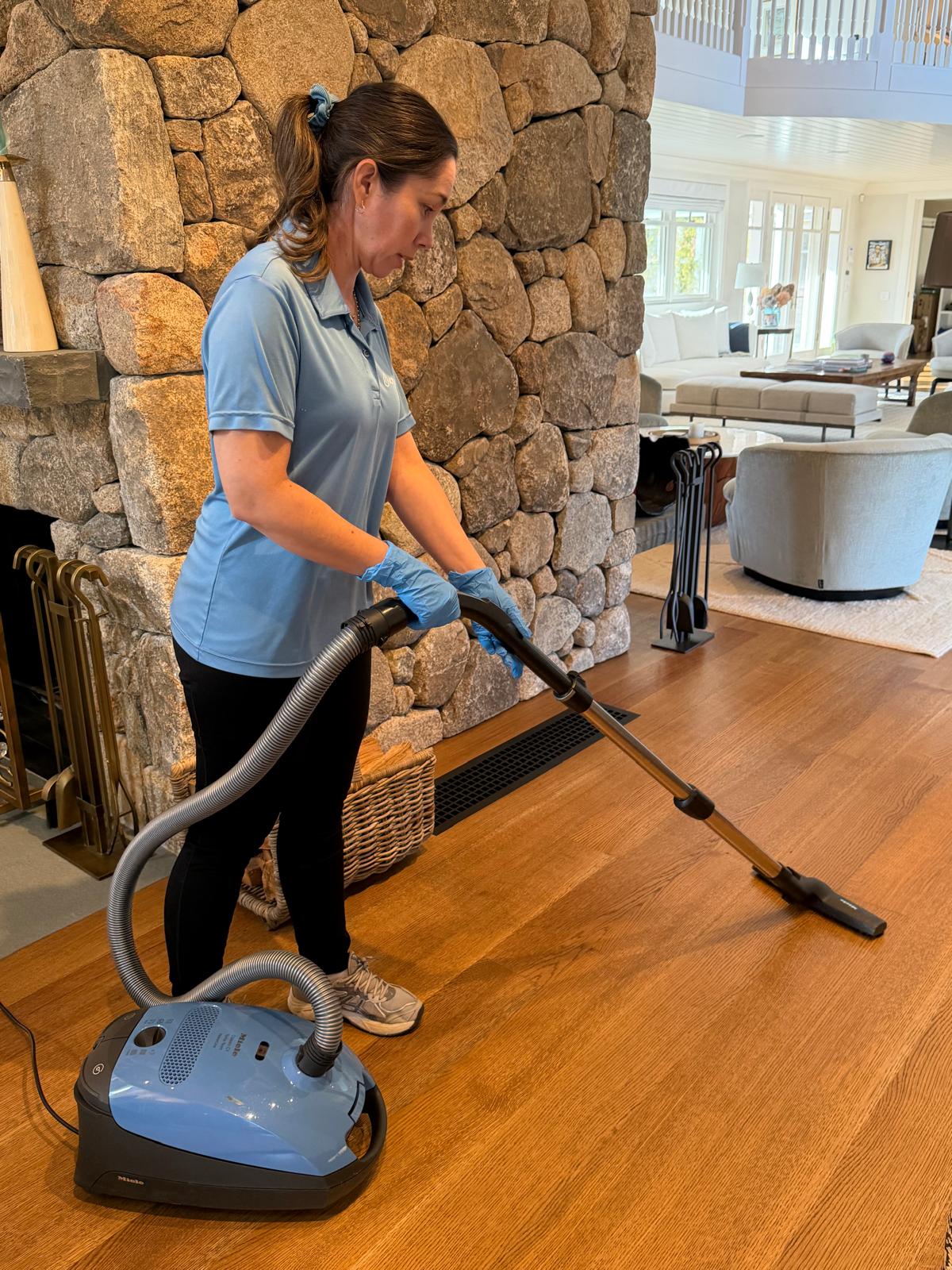 ICP Cleaning Services specialist vacuuming hardwood floor by stone fireplace in Martha's Vineyard home