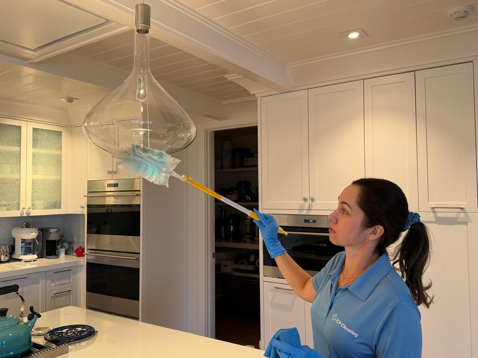 ICP Cleaning team member dusting custom glass pendant light fixture in kitchen