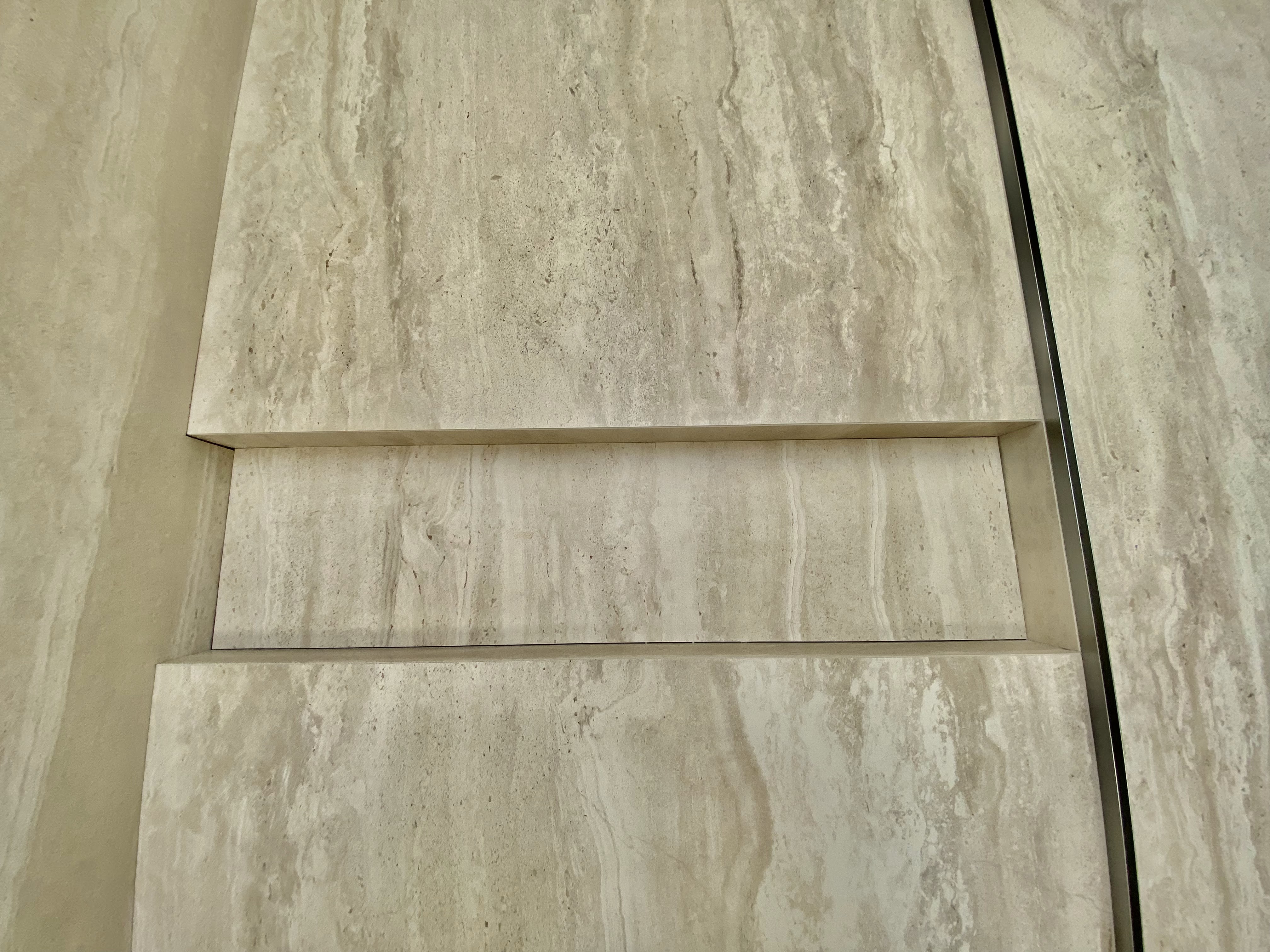 Precision travertine stone wall tiling with clean recessed niche detail and architectural mitred junctions.