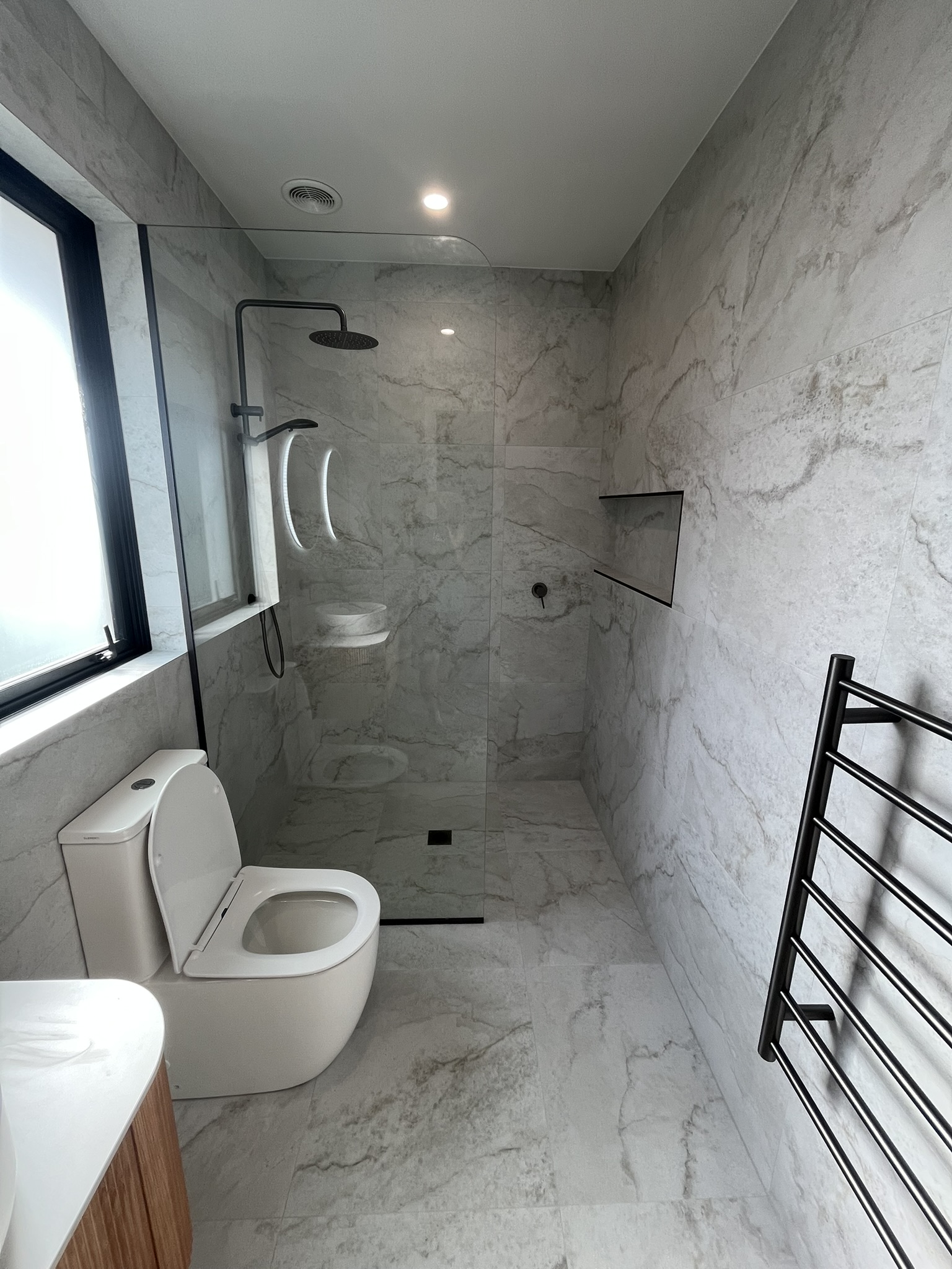 Luxury grey marble walk-in shower with minimalist frameless glass and black fittings.