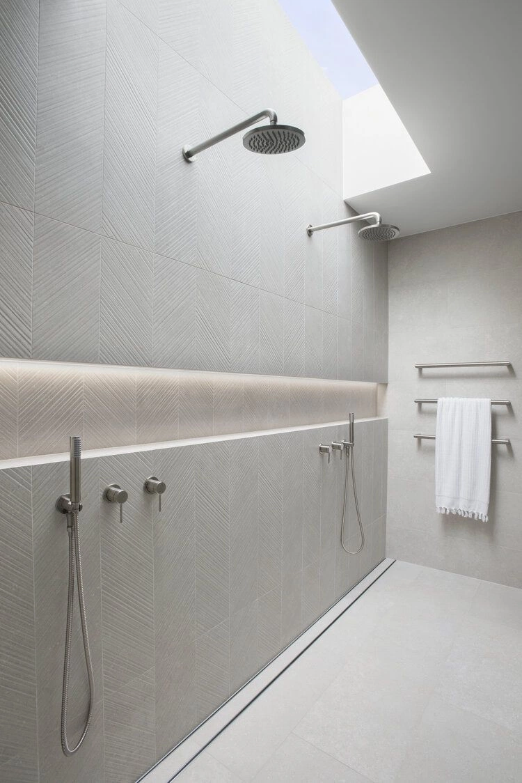 Luxury walk-in shower with textured herringbone grey tiling, dual rain heads, and integrated recessed lighting.