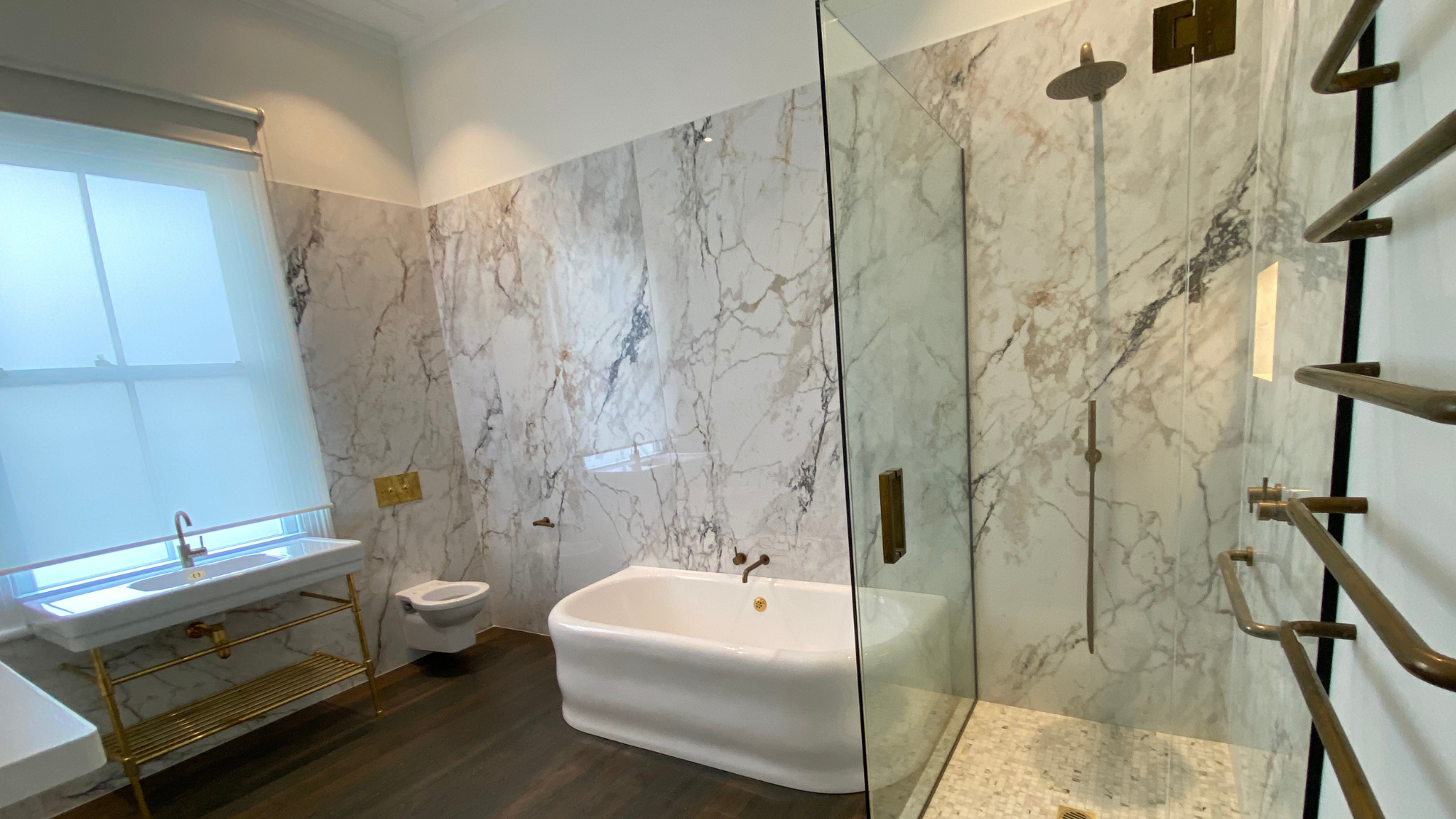Luxury Auckland bathroom with bookmatched marble wall tiling, freestanding tub, and walk-in shower.