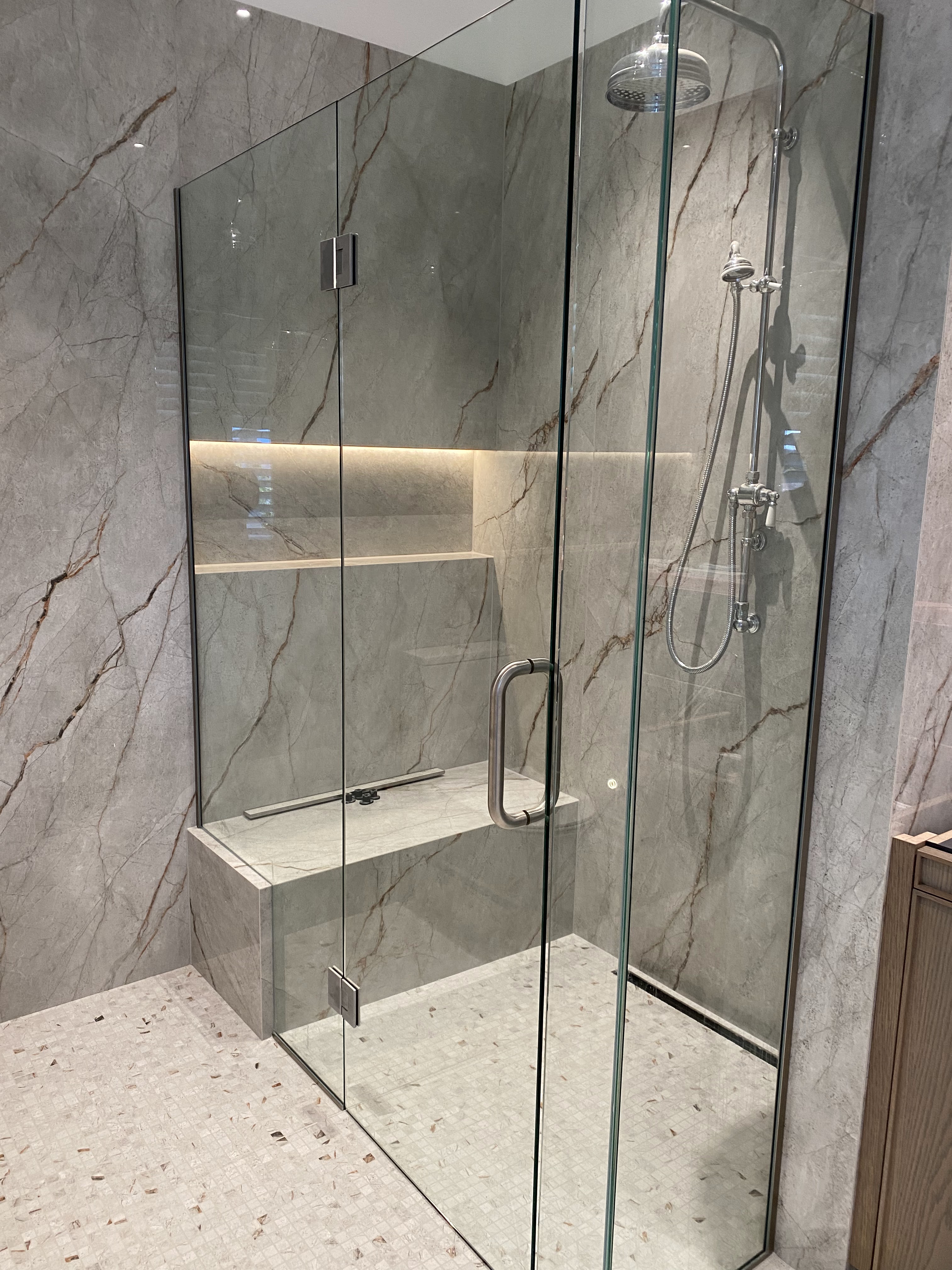 Custom tiled walk-in shower with marble slab walls, integrated tiled bench, illuminated niche, and frameless glass.