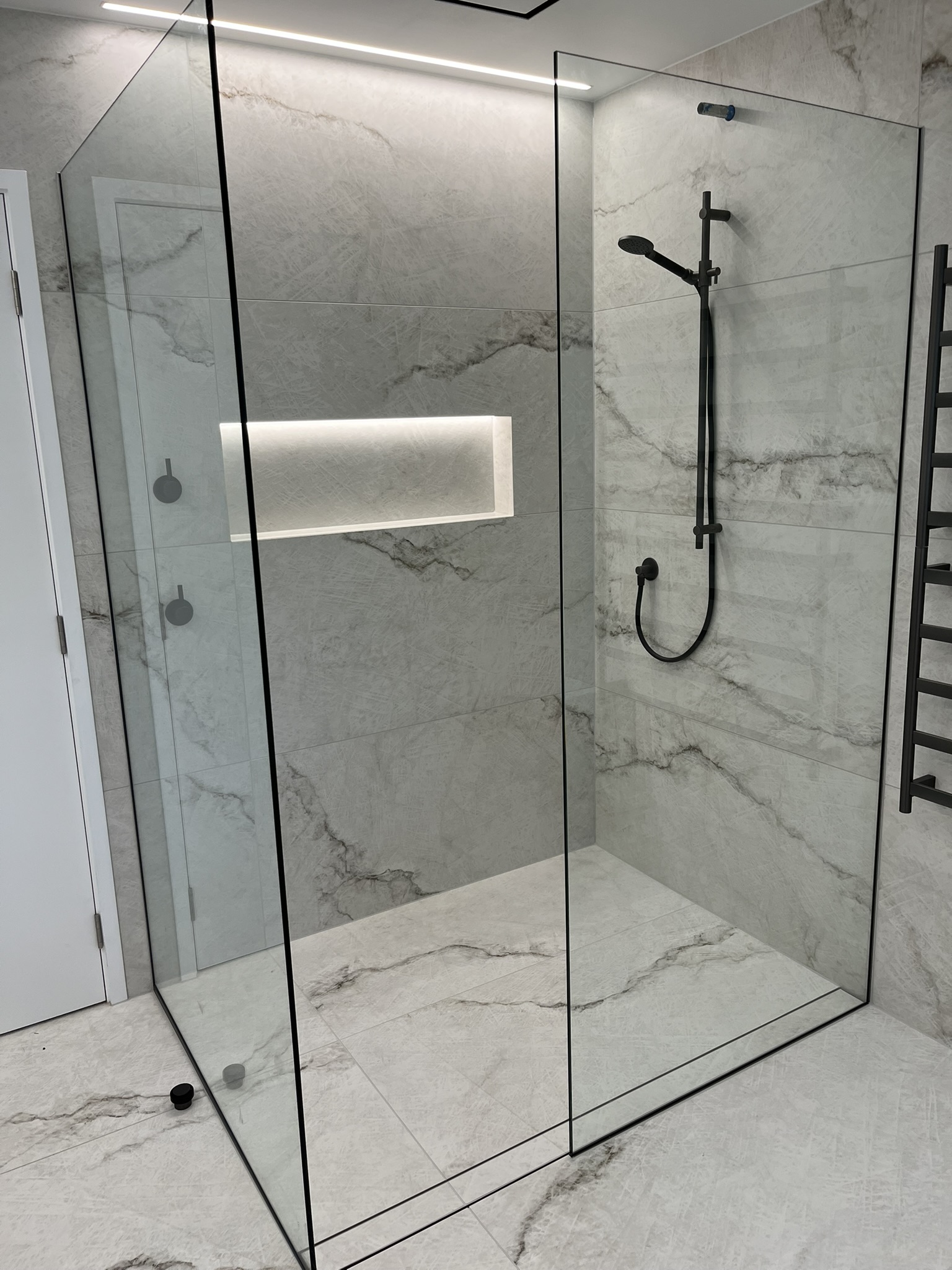 Custom walk-in shower with large-format marble tiles, illuminated niche, and matte black tapware.