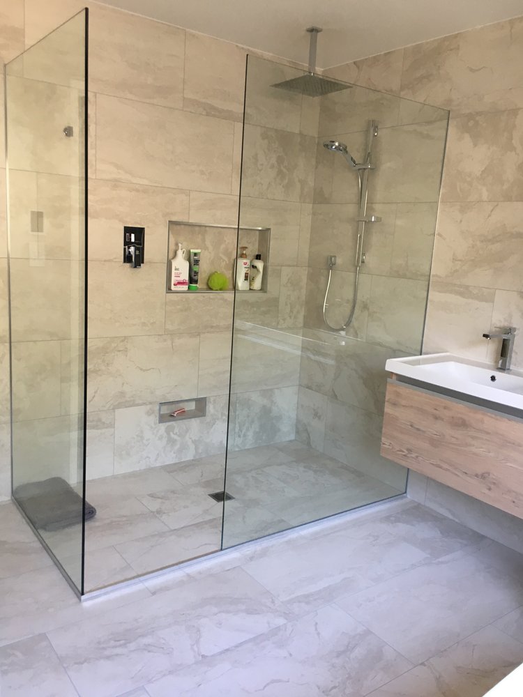 Level-entry walk-in shower with neutral stone tiles, frameless glass, and recessed niche.