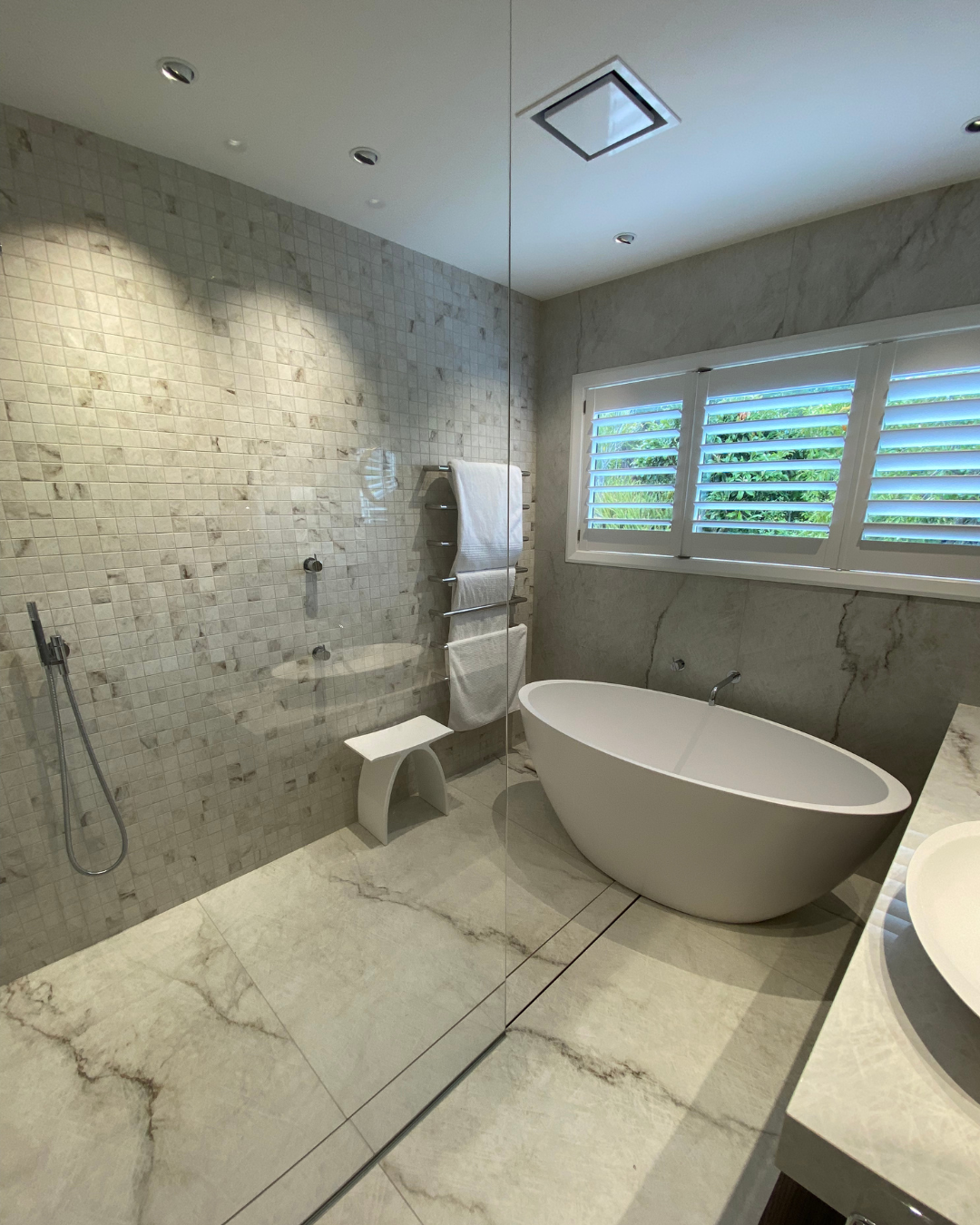 Luxury wet room bathroom with freestanding tub, mosaic feature wall, marble flooring, and glass divider.