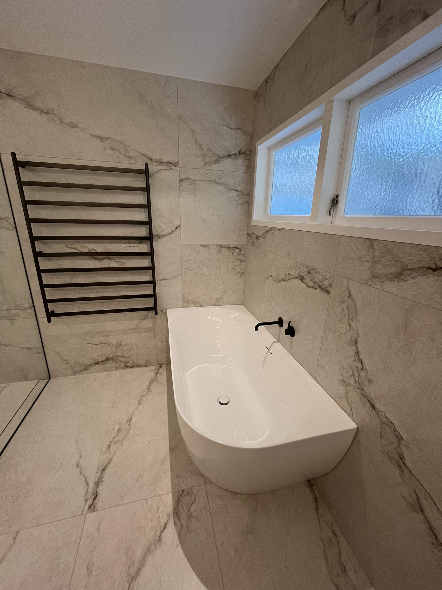 Precision tiled bathroom wall and floor surround with freestanding tub and black hardware.