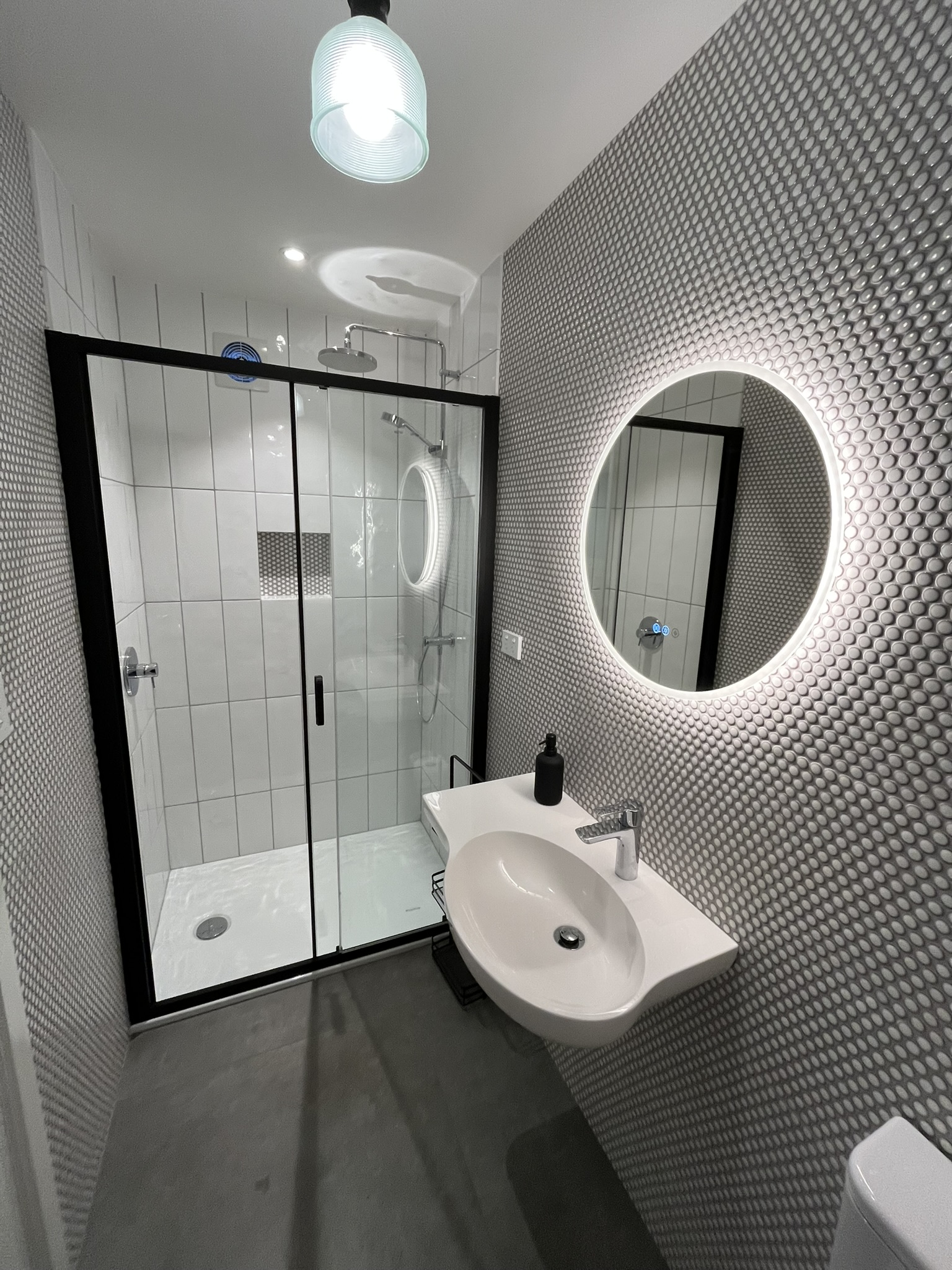 Detailed feature mosaic wall tiling with walk-in shower and illuminated round mirror.