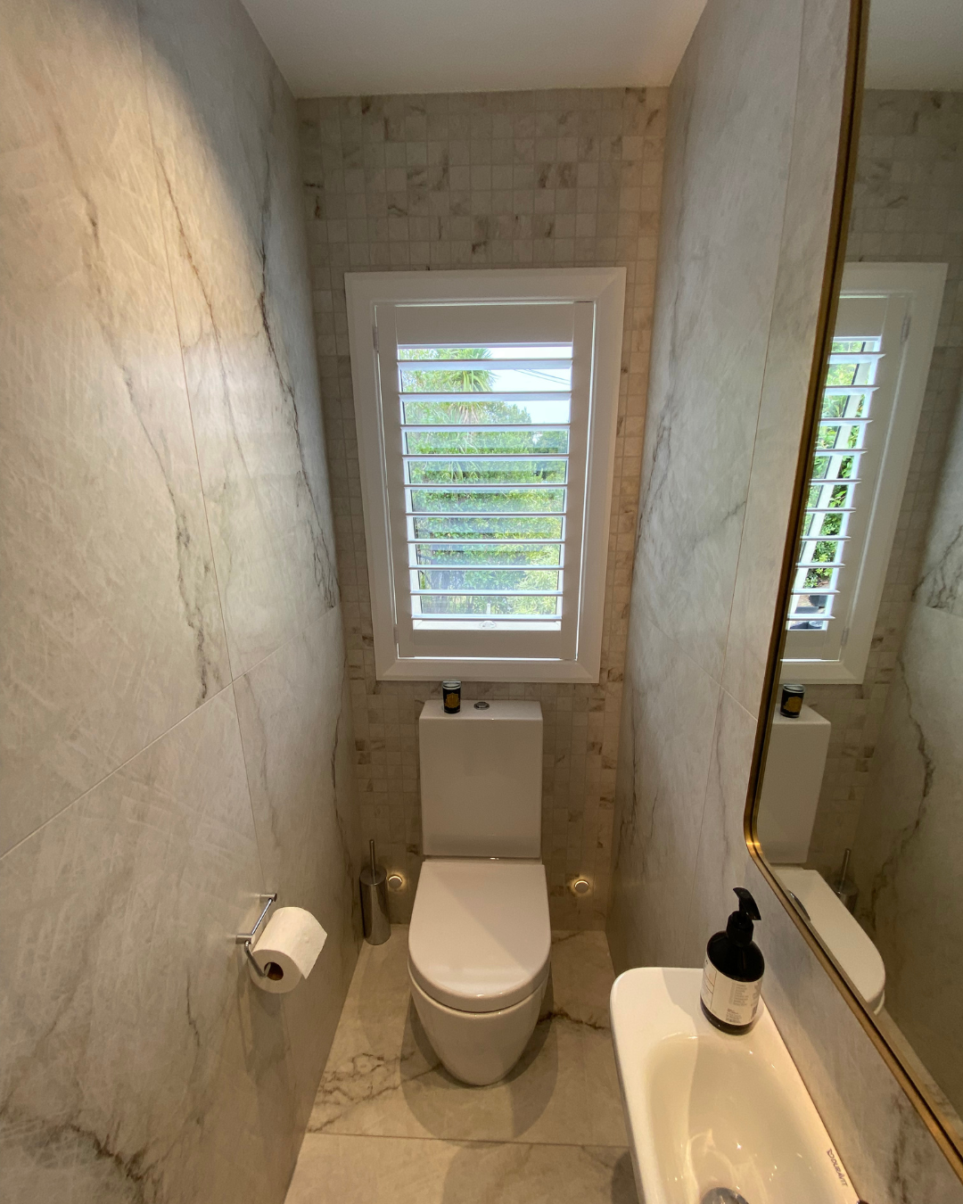 Marble tiled powder room with vanity, mirror and louvered window.