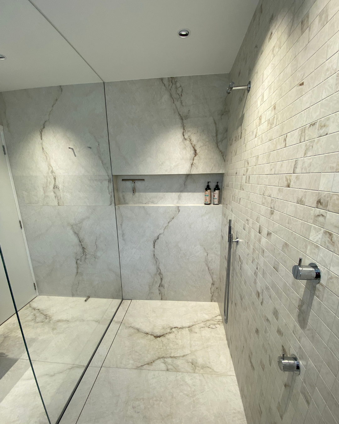 Large marble slab wall and floor tiles with small mosaic shower wall and flush drainage channel.