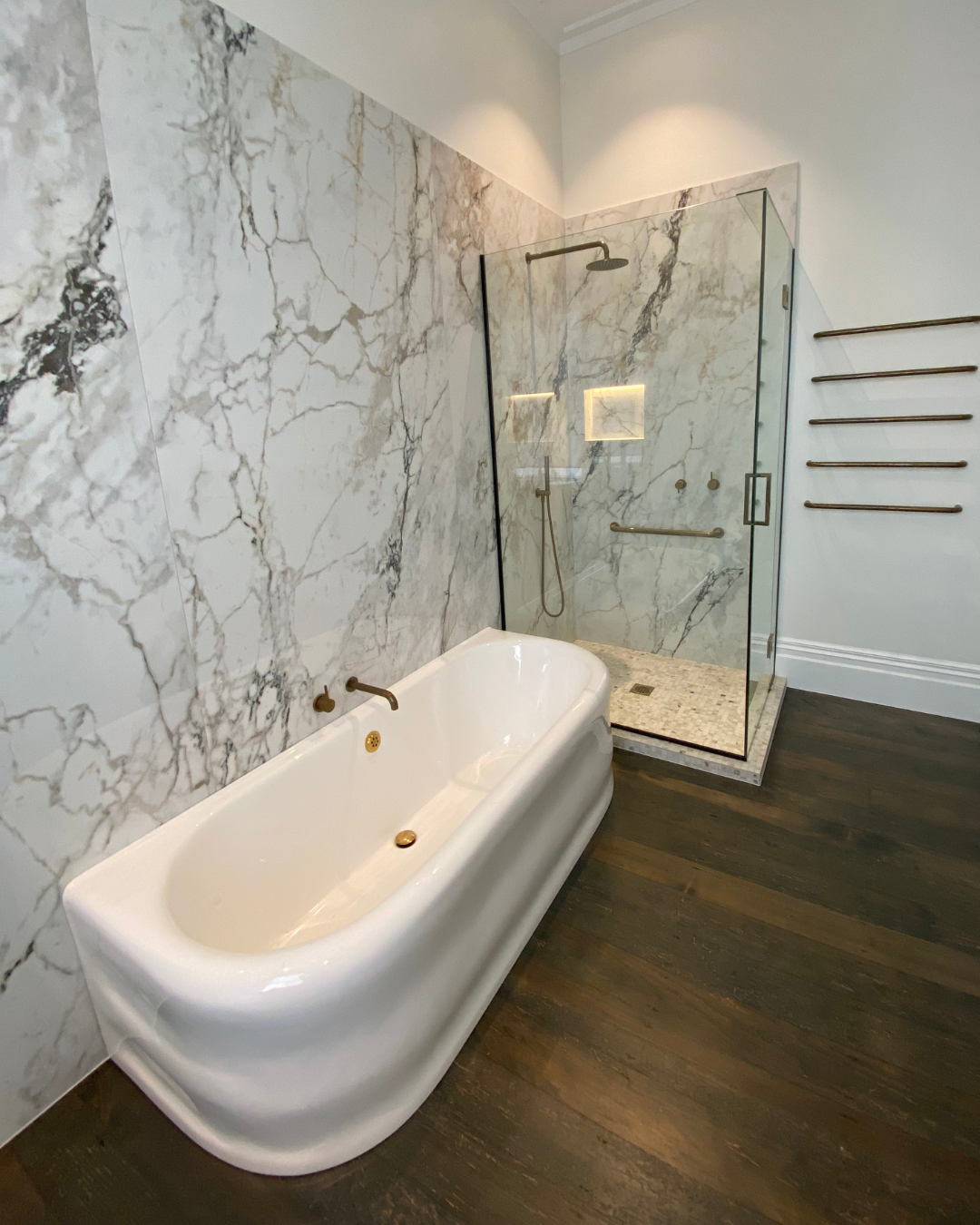 Freestanding bathtub against marble slab feature wall and glass shower enclosure.