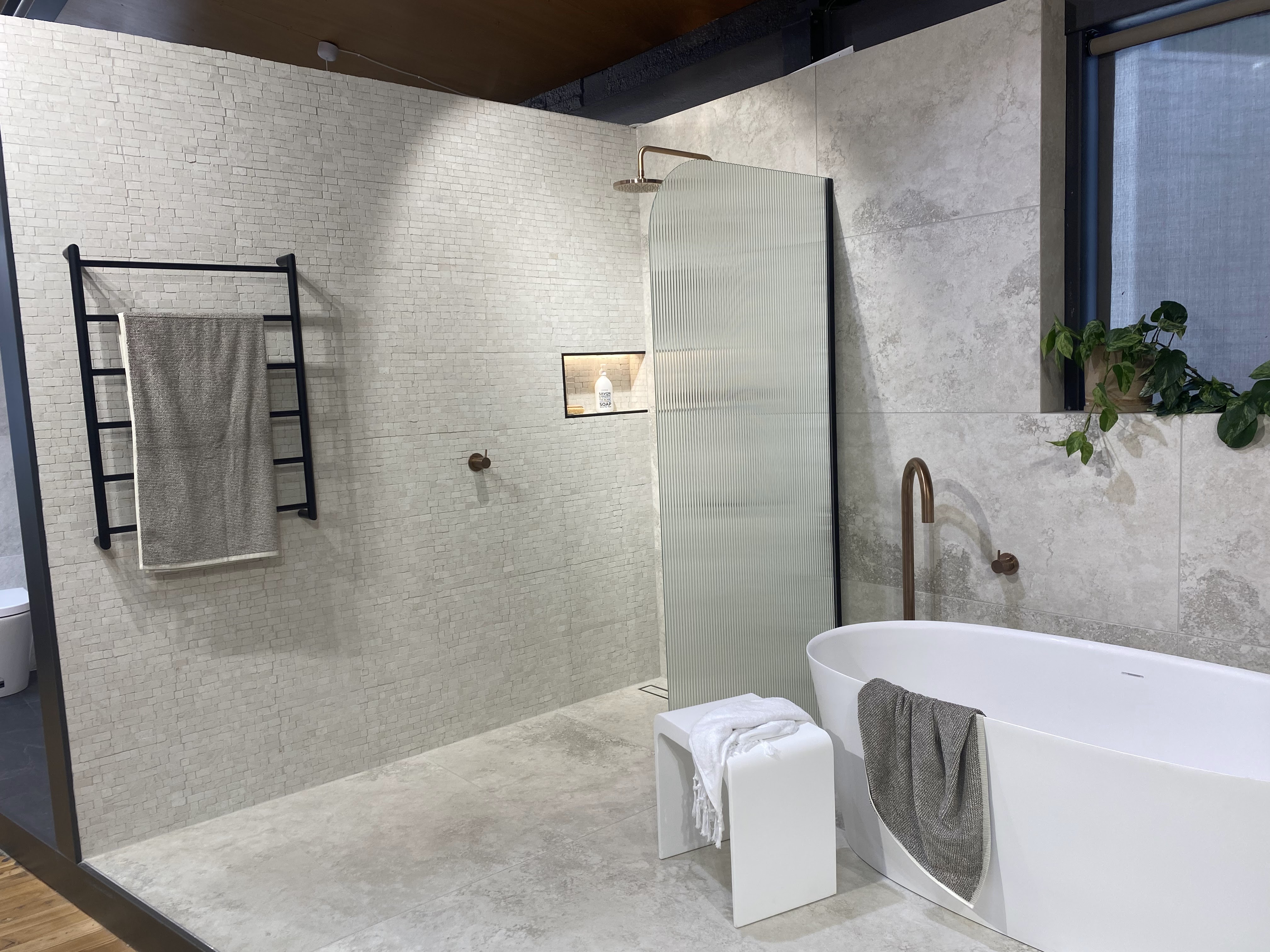Luxury bathroom with freestanding tub, fluted glass shower screen, and mosaic tiled walls.
