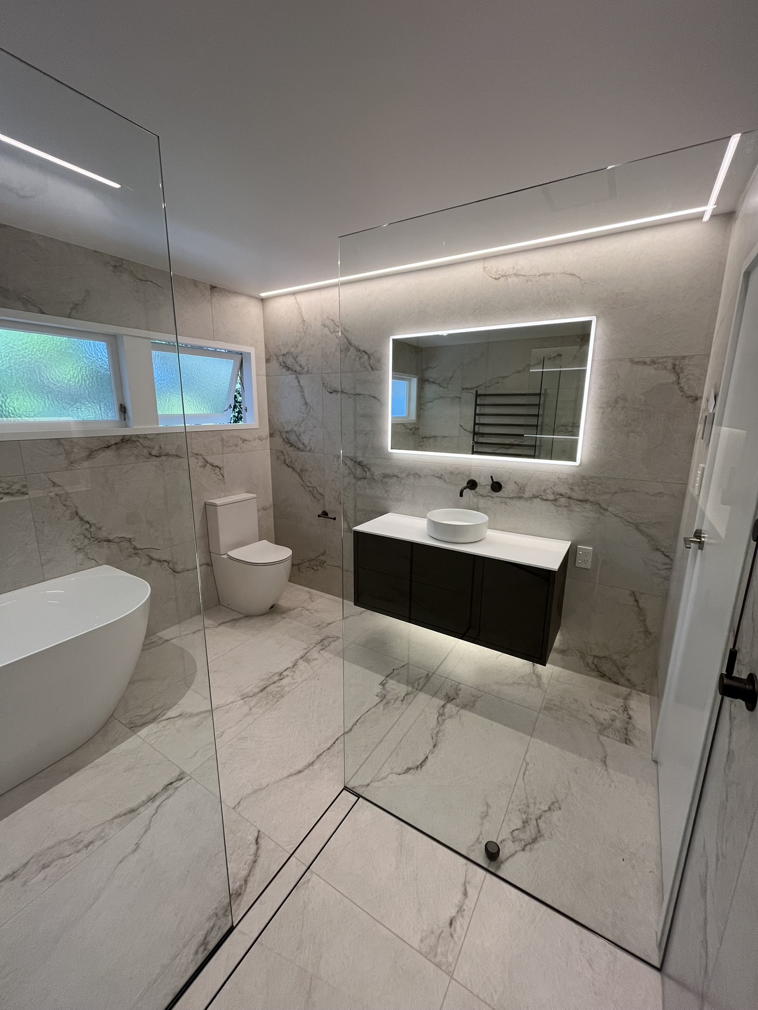 Luxury full residential bathroom tiled in large-format porcelain with flush floor channel.