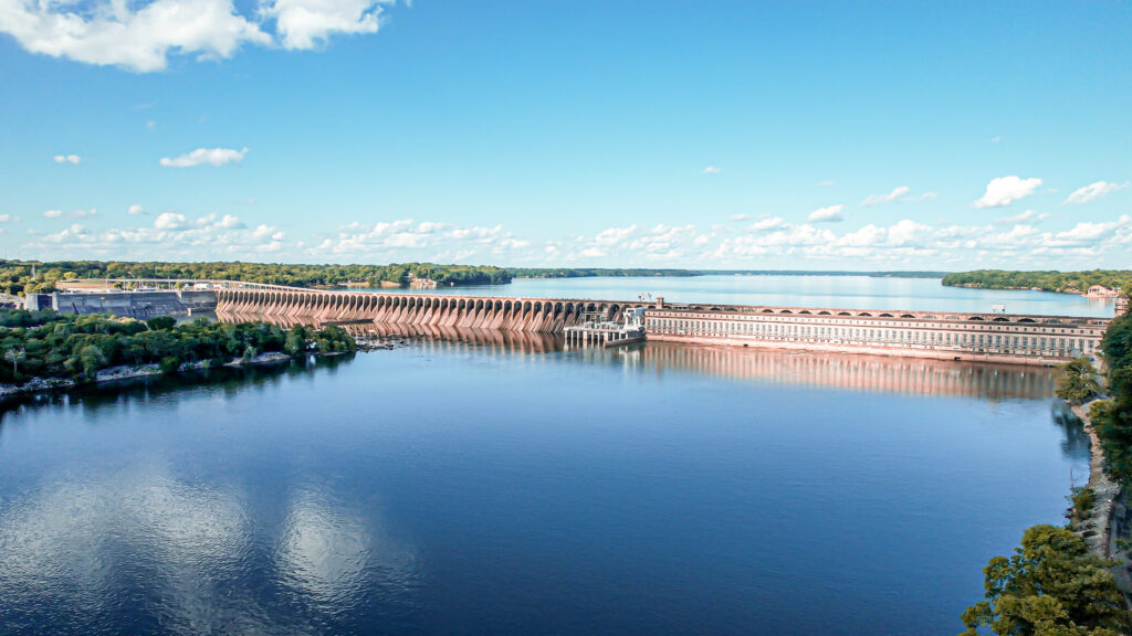 Aerial view of the Wilson Dam spanning the Tennessee River in Florence, AL, with lush greenery on the banks.