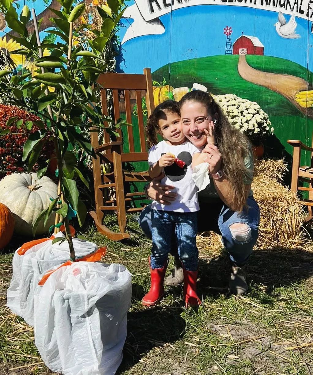 Mother and daughter posing happily next to fresh fruit trees and pumpkins in front of the farm barn mural