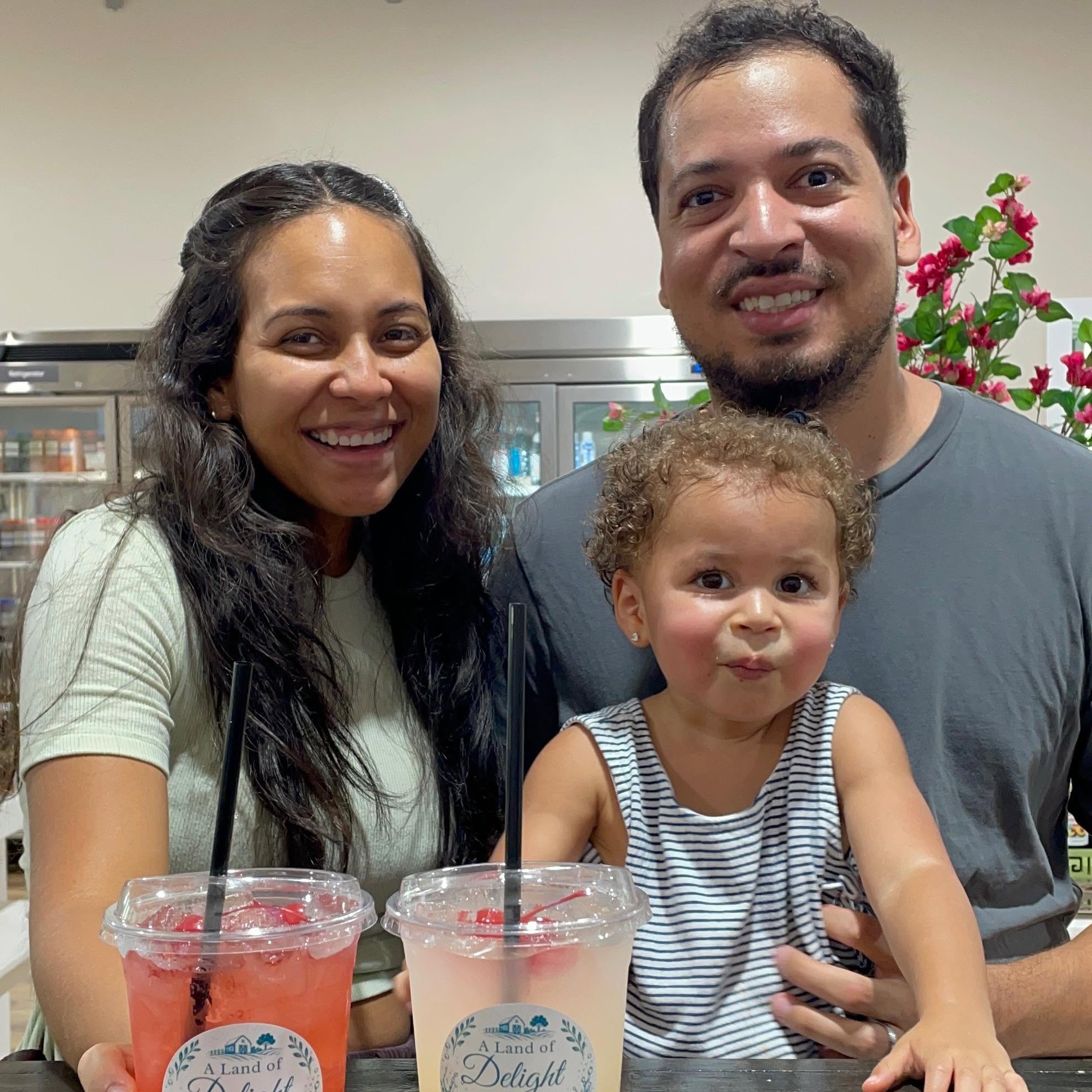Smiling family with their toddler enjoying fresh handcrafted fruit sodas with farm logo cups at the Harvest House Cafe