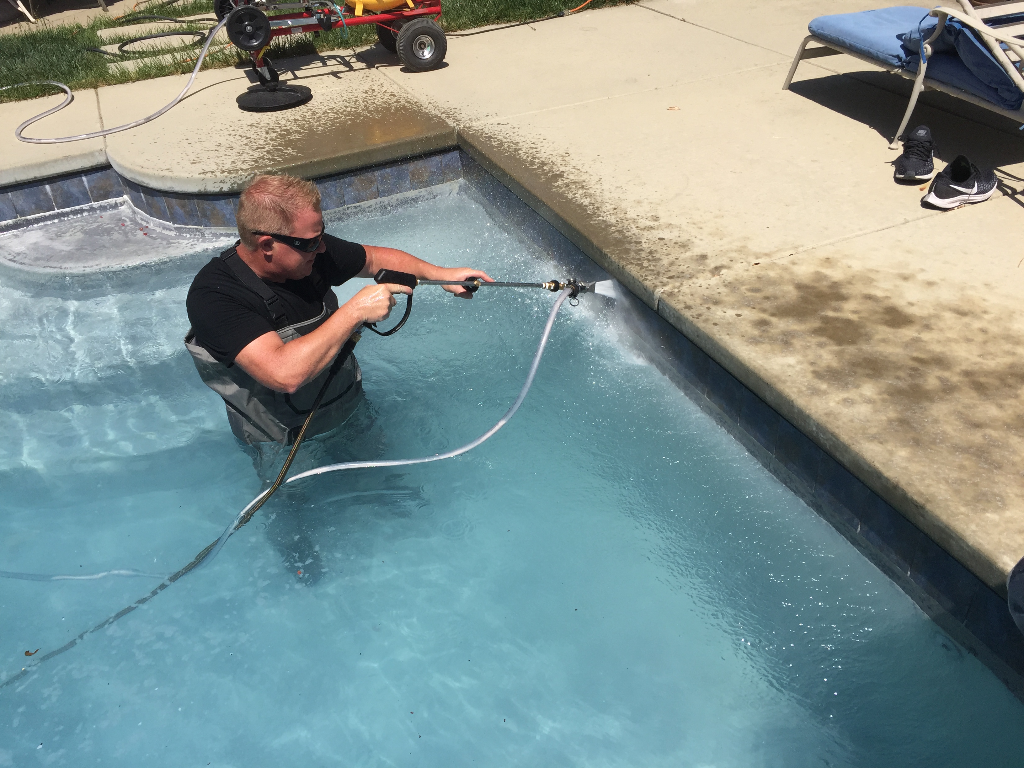 Technician pressure washing waterline pool tile