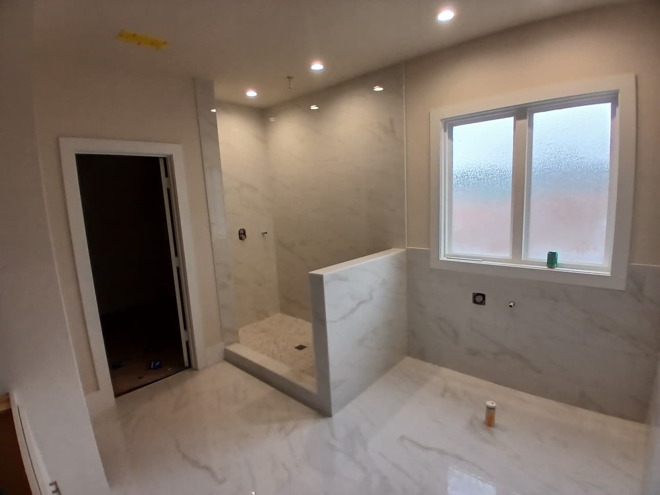 Expansive master bathroom renovation with large-format white marble porcelain tile, tiled pony wall shower, and frosted privacy window in Seneca SC