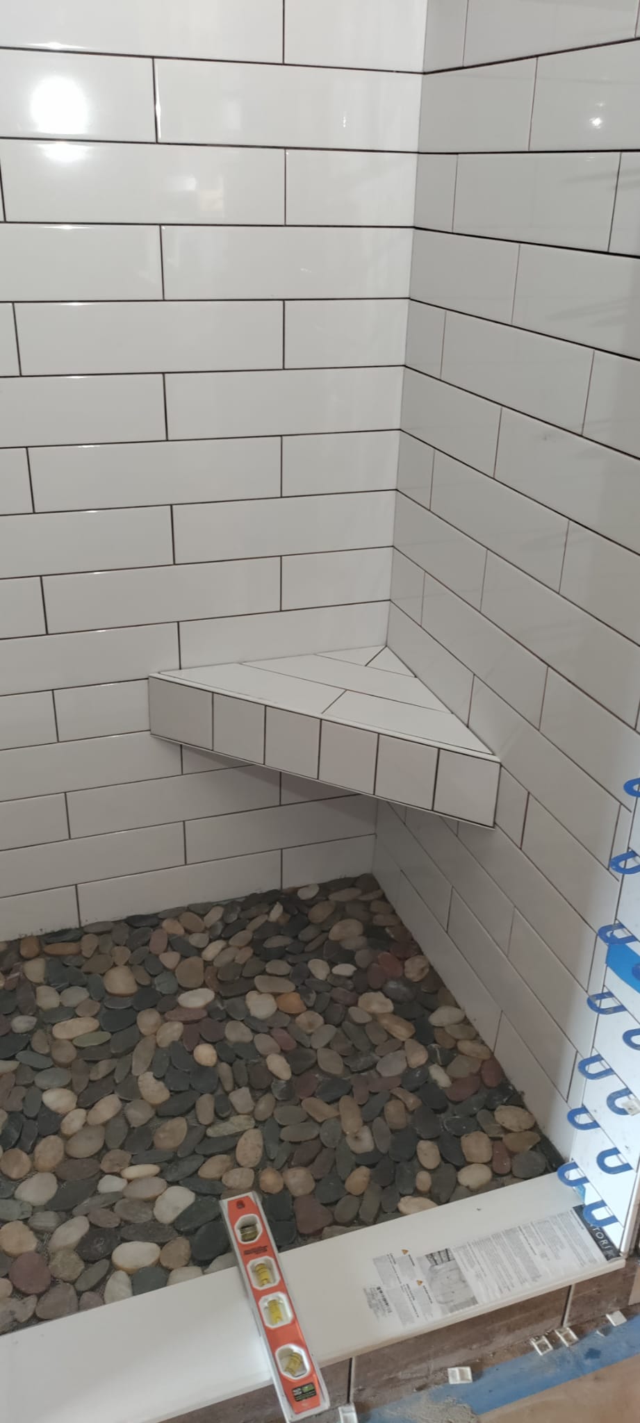 White subway tile shower with natural river rock pebble floor and custom tiled corner shaving bench in Anderson SC by Roberto Vicente