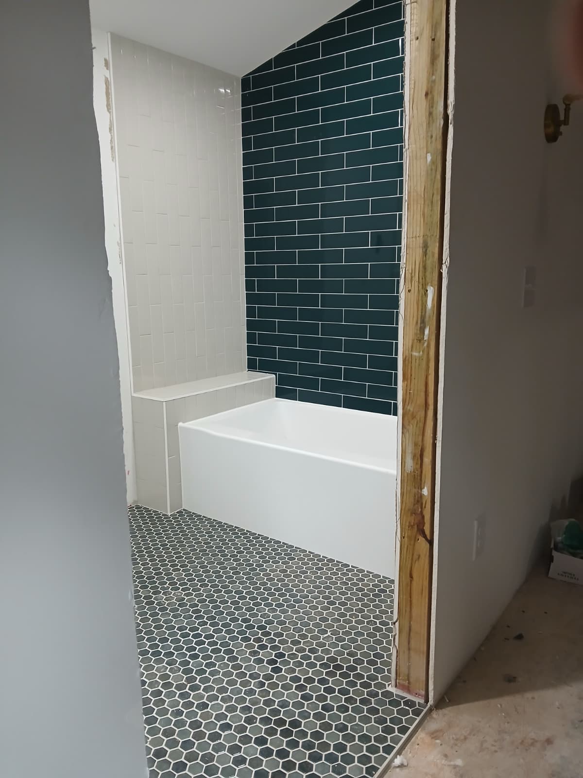 Deep emerald green subway tile accent wall with white soaking tub, vertical tile ledge, and dark hexagon floor tile by Roberto Vicente in Greenville SC