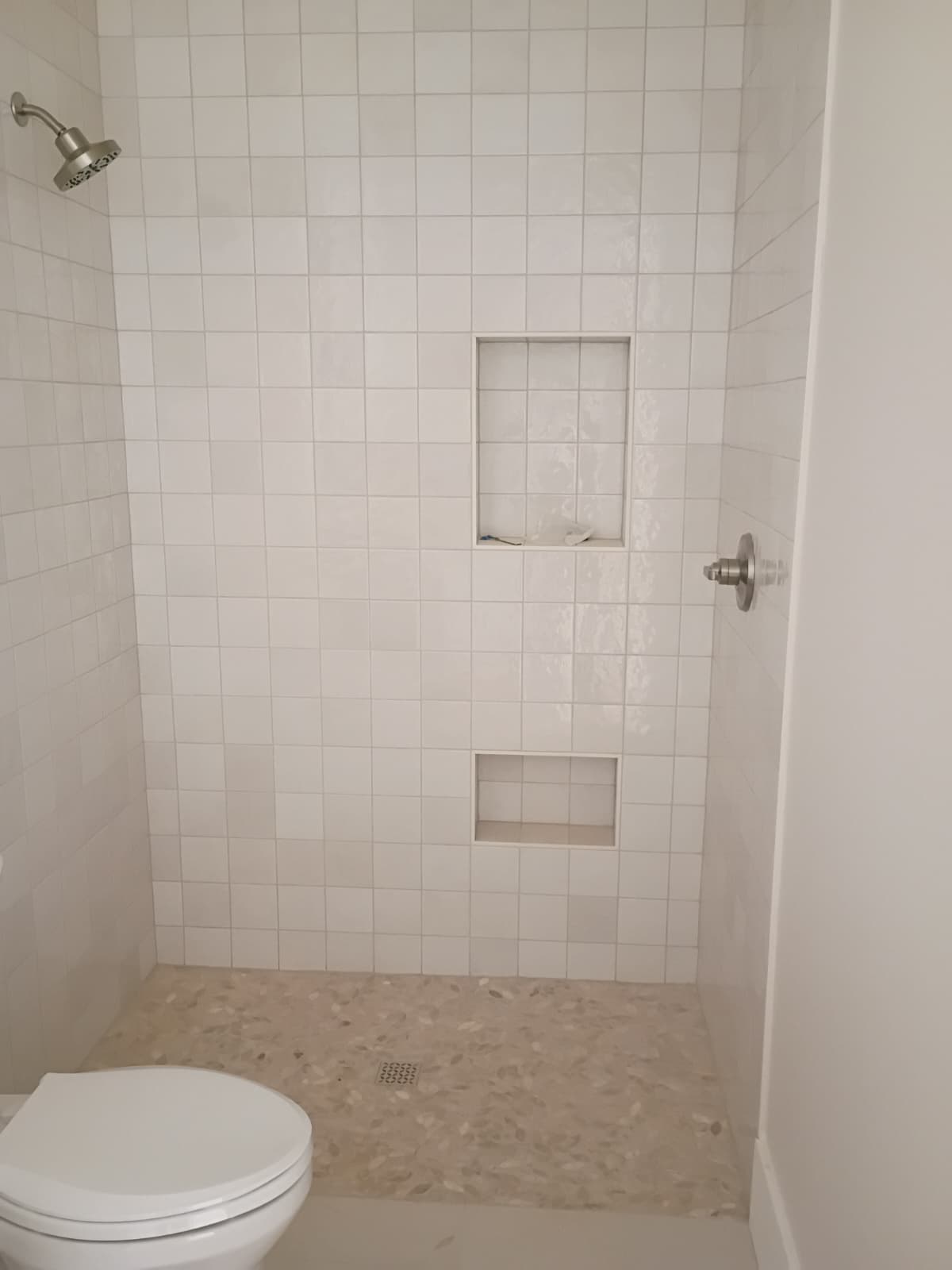 Finished white artisan grid tile walk-in shower with upper and lower recessed niches, pebble shower floor, and brushed nickel hardware in Seneca SC
