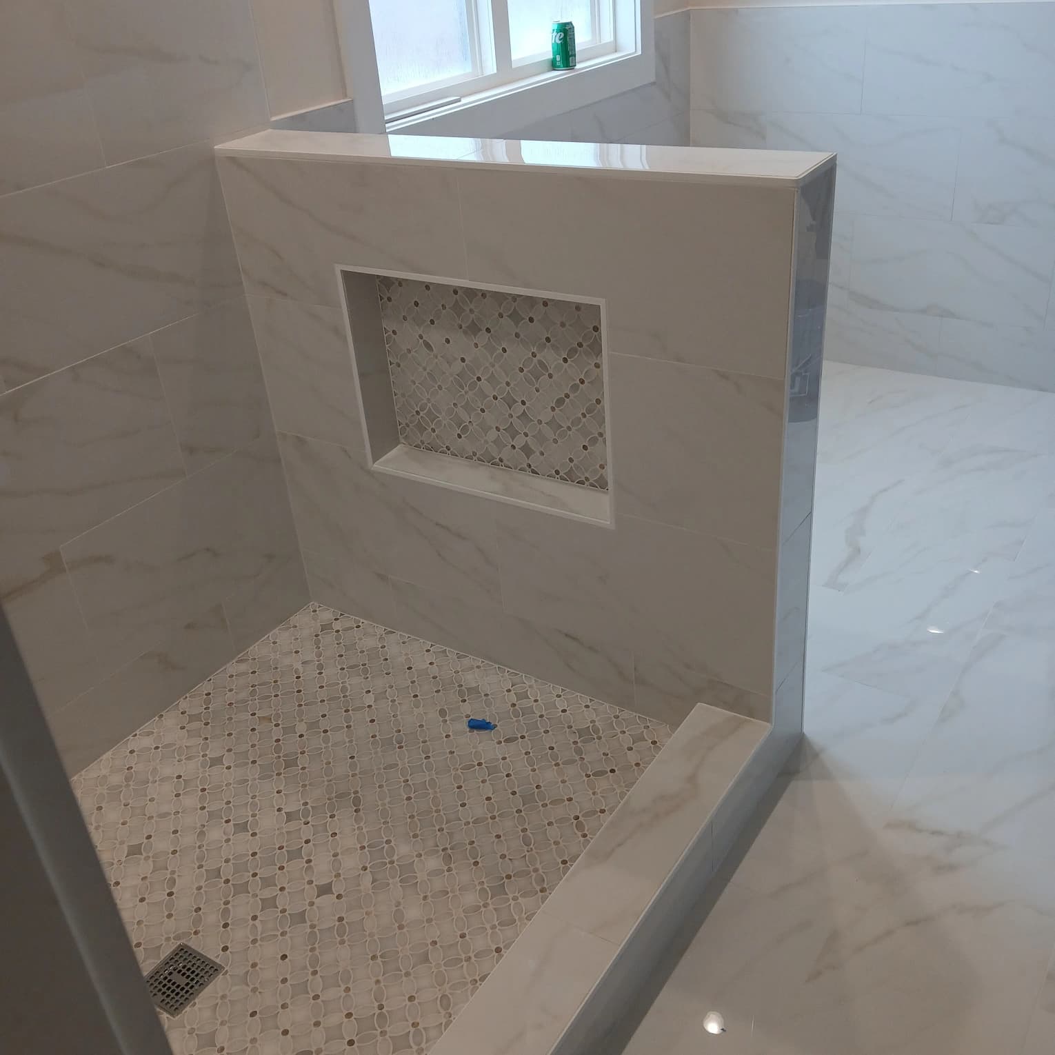 Custom marble tile walk-in shower with tiled pony wall, solid sill cap, geometric mosaic niche, and matching mosaic floor by Roberto Vicente