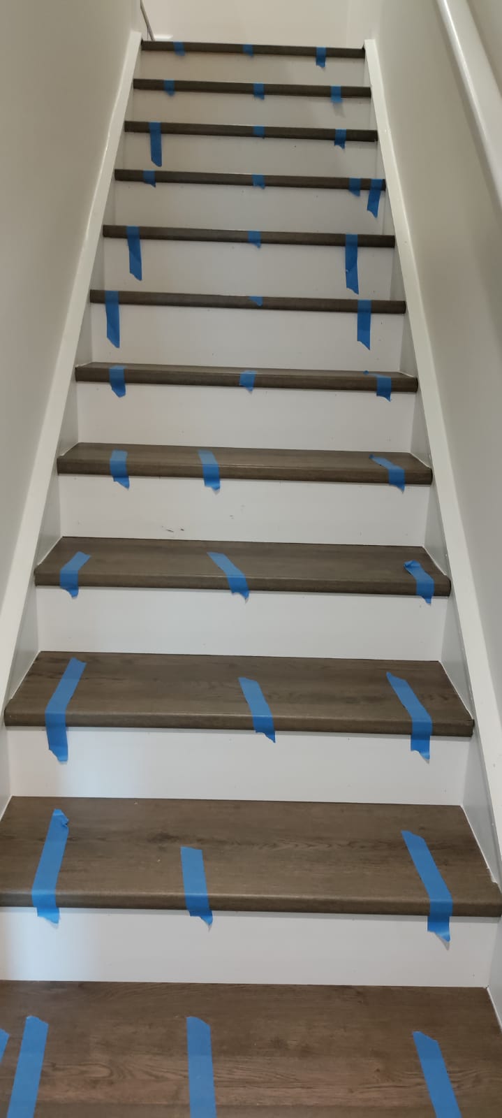 Precision luxury vinyl plank stair tread install with painted white risers during curing process by Roberto Vicente in Greenville SC