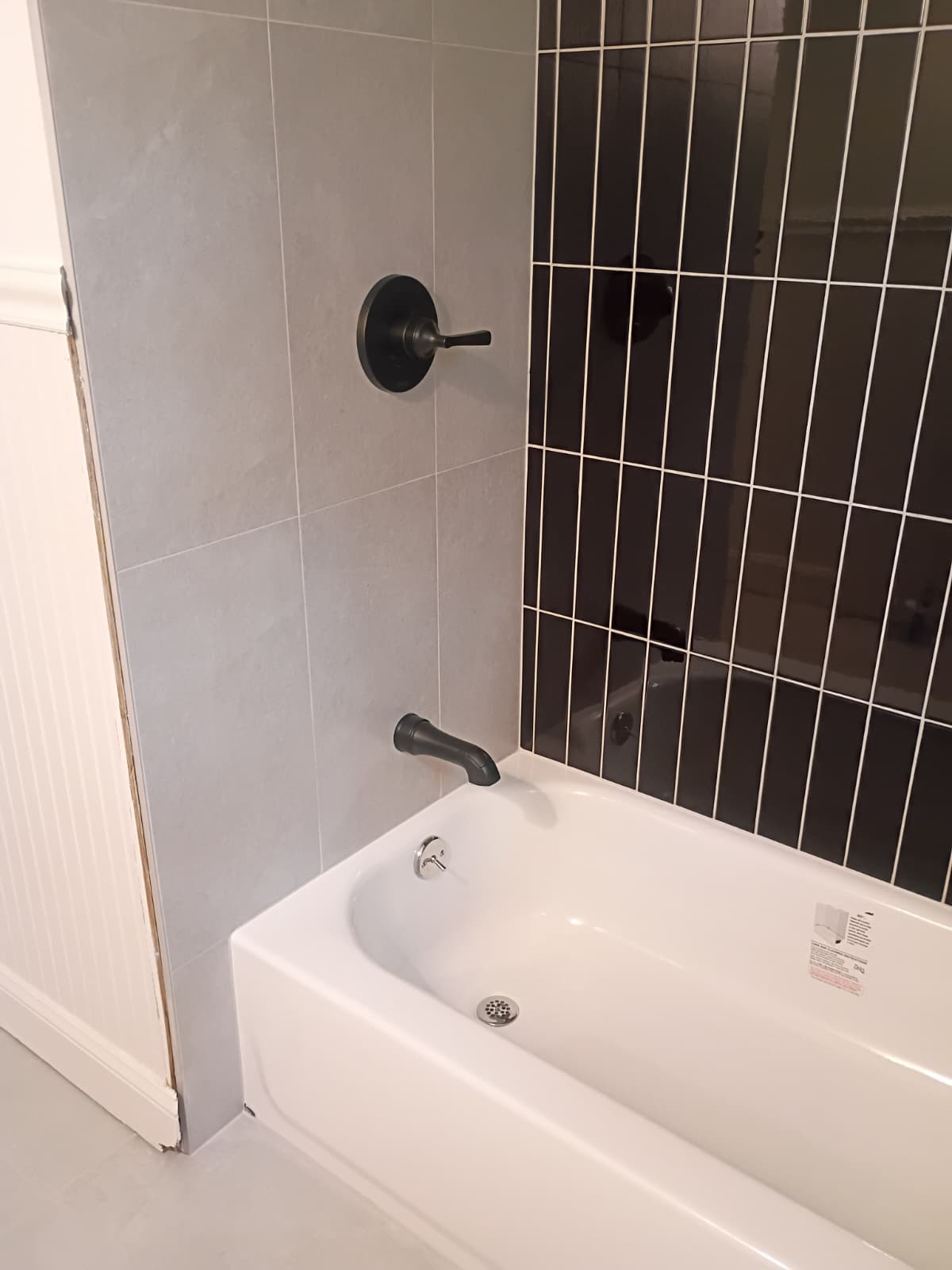 Modern tub surround with vertical gloss black subway tile, gray porcelain side walls, and matte black plumbing fixtures in Easley SC