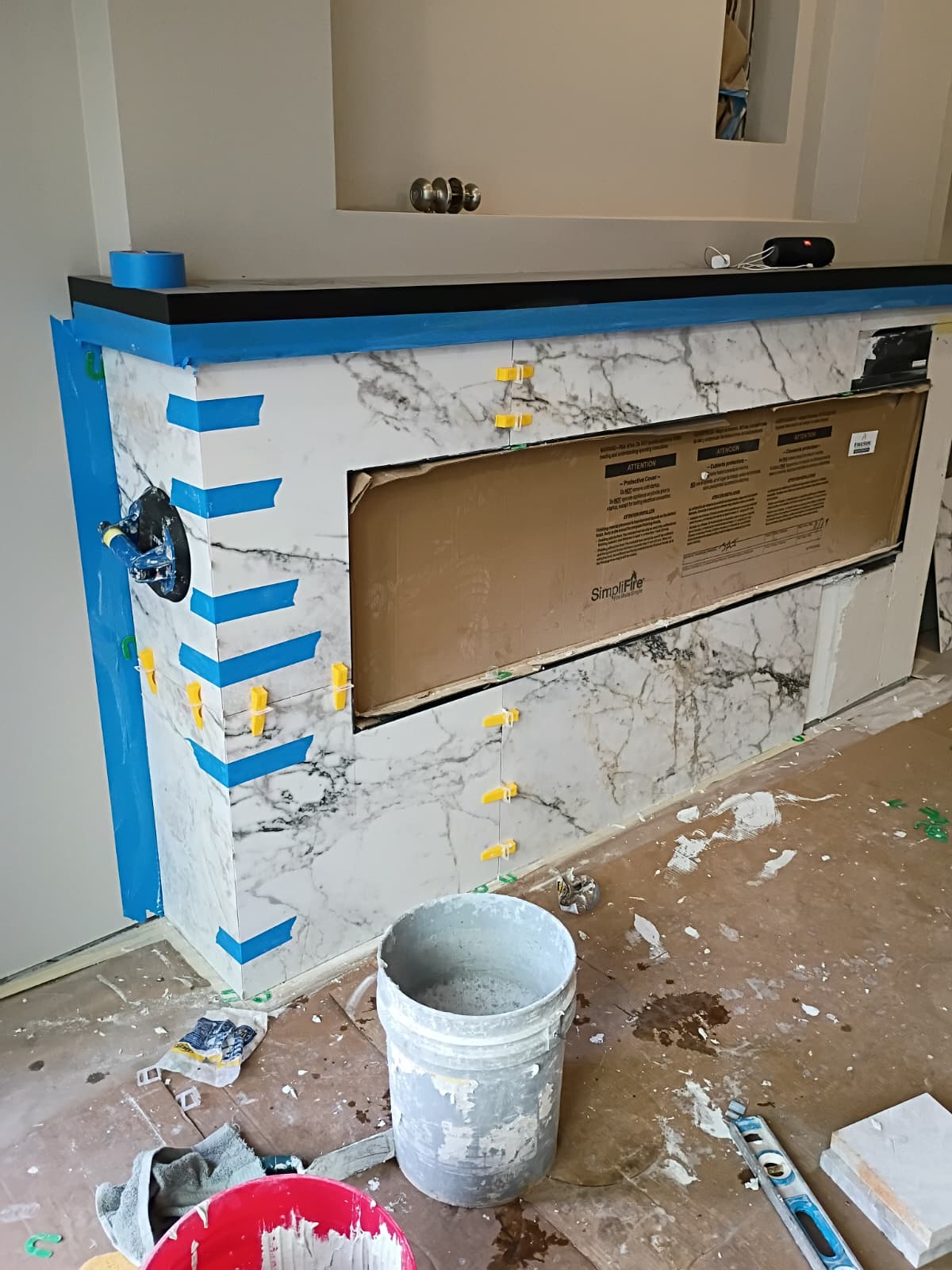 SimpliFire linear electric fireplace marble tile surround under construction with leveling spacers and suction cups in Greenville SC