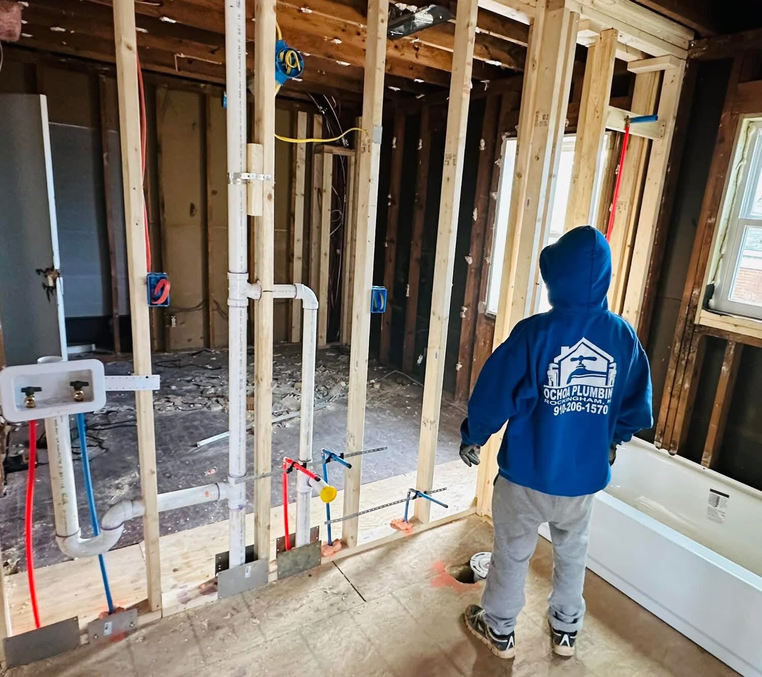 Trabajador de Ochoa Plumbing con sudadera azul de la empresa, instalando tubería nueva en una pared abierta