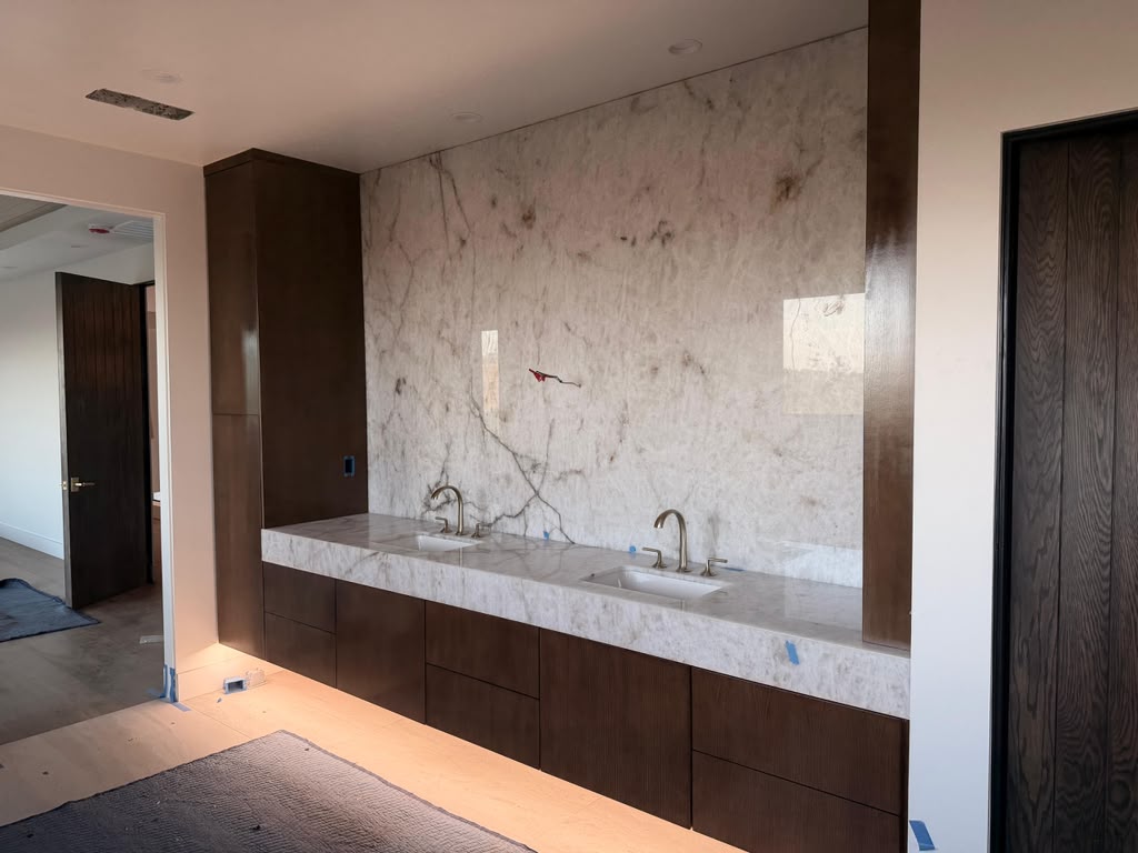 Modern floating dark walnut dual vanity suite with full-height marble slab backsplash and warm LED underglow in Coronado CA