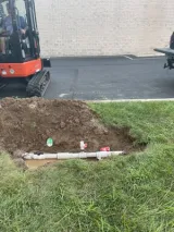 Underground sprinkler line dug up and exposed for repair next to a mini excavator