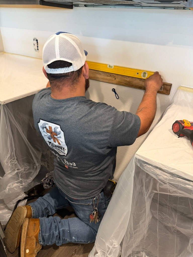 Manny leveling a kitchen project with precision in his branded Manny The Handyman shirt