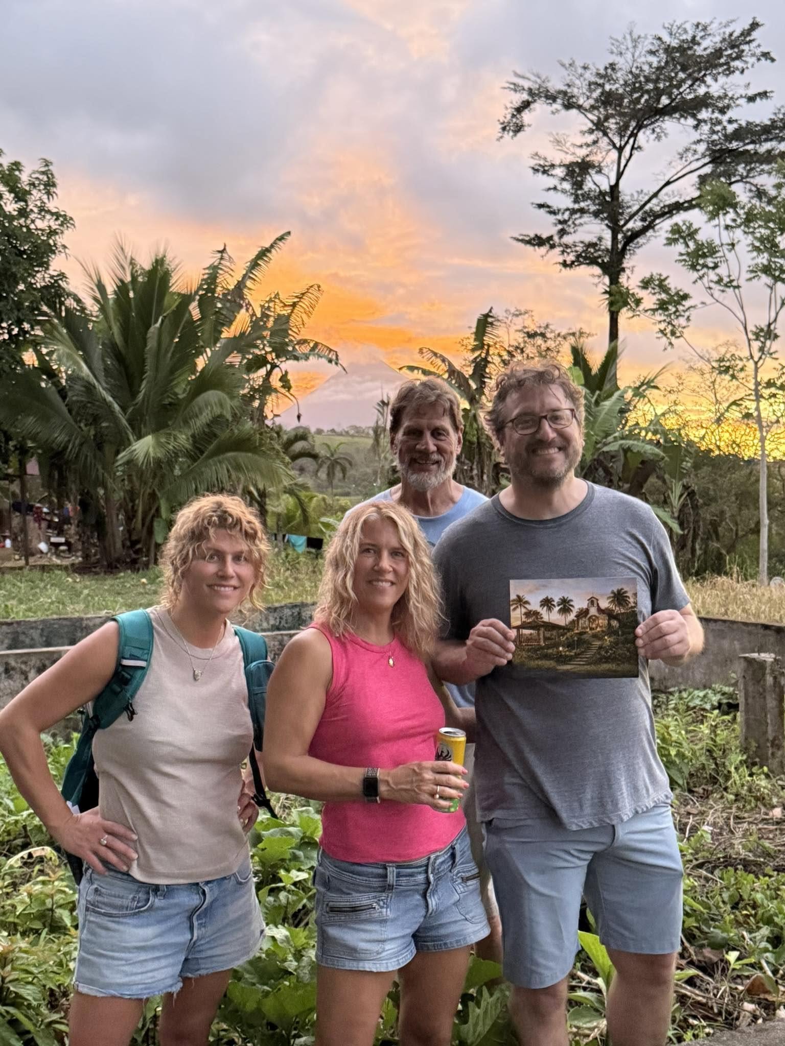 The family holding a rendering on the property at sunset with Arenal Volcano in the background
