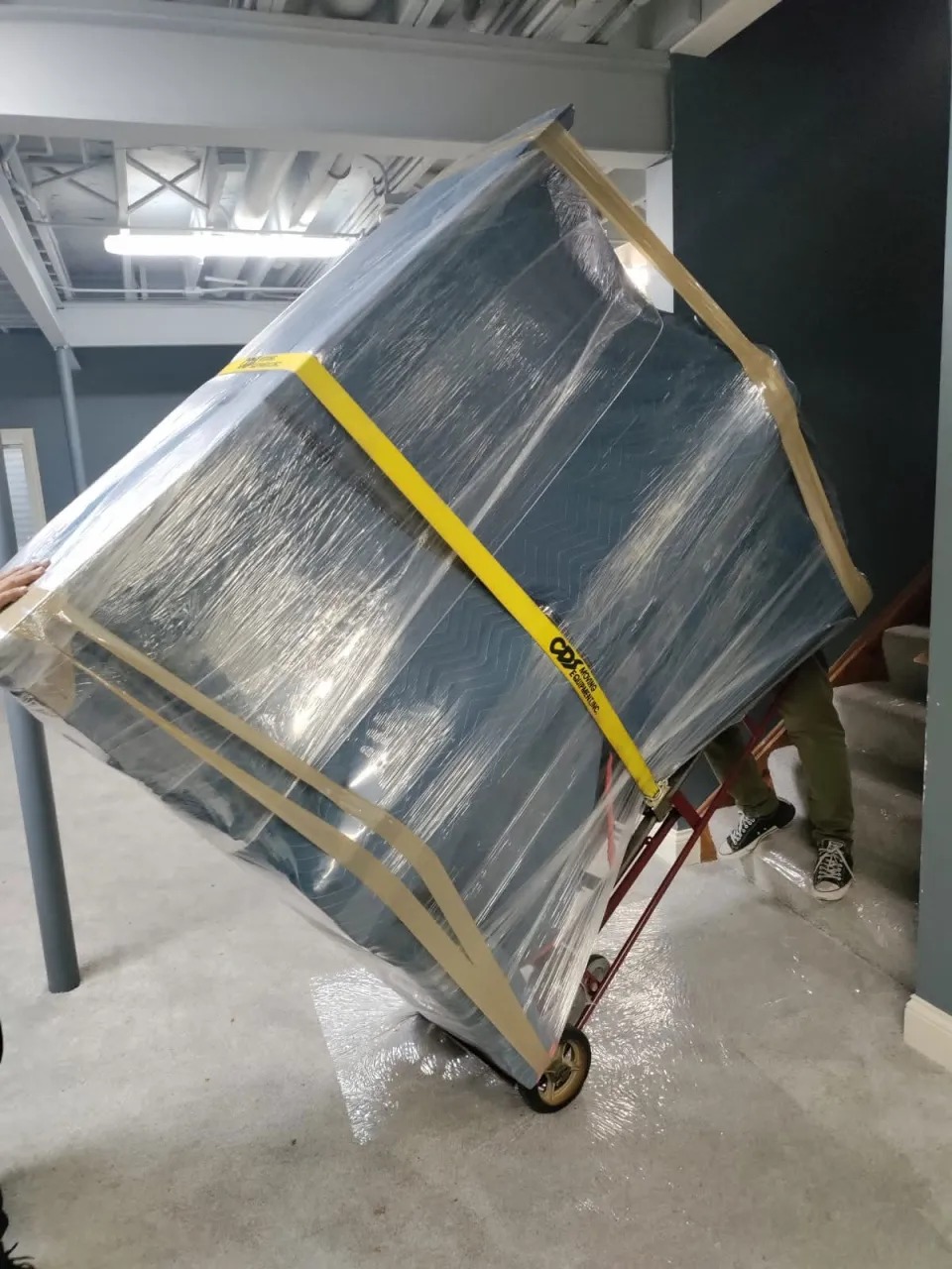 Mover wheeling strapped furniture on a hand truck down basement steps in Bolingbrook