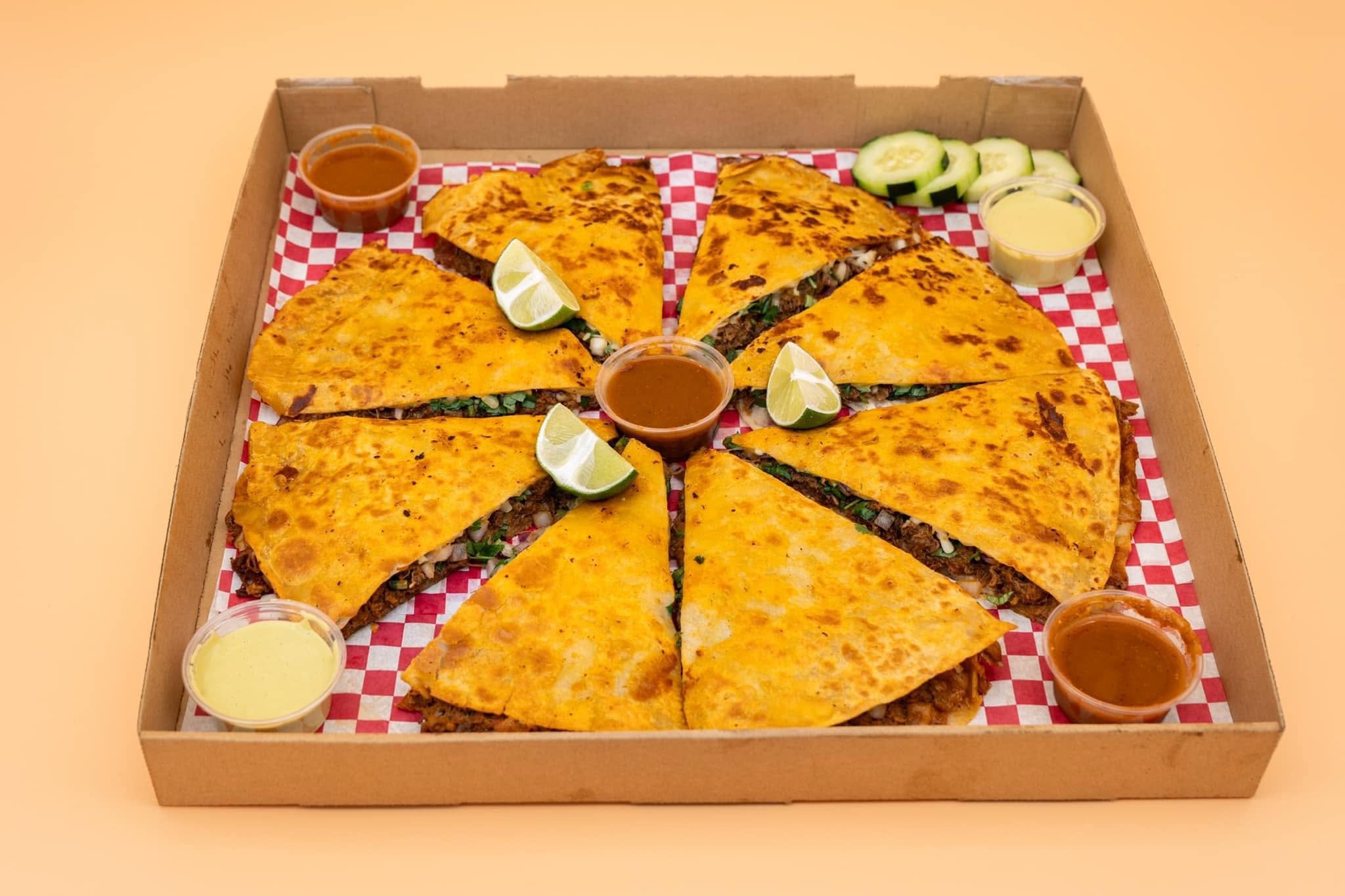 Pizza Birria artesanal cortada en rebanadas con limones y salsas