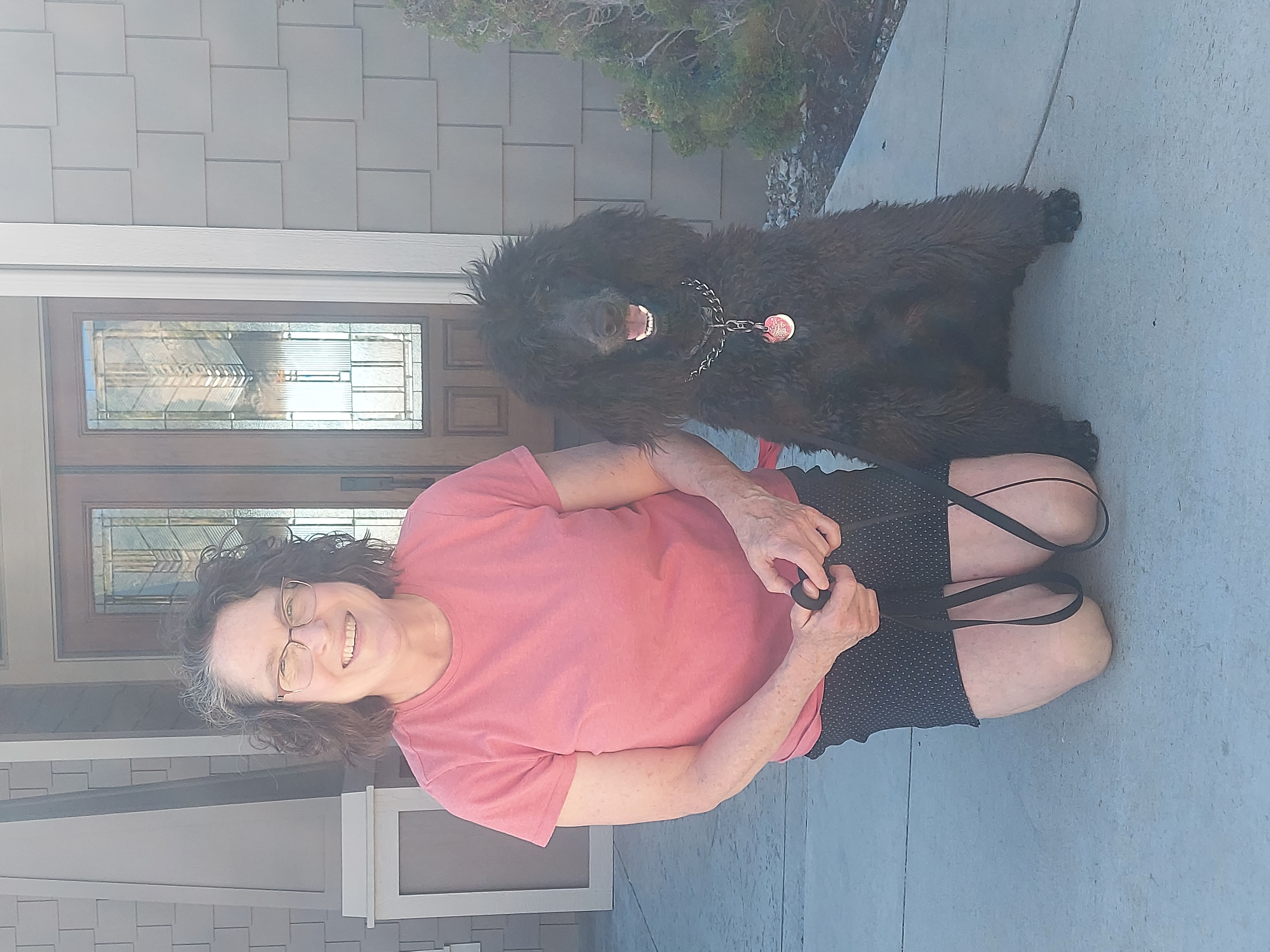 Smiling woman kneeling outdoors with attentive black companion dog