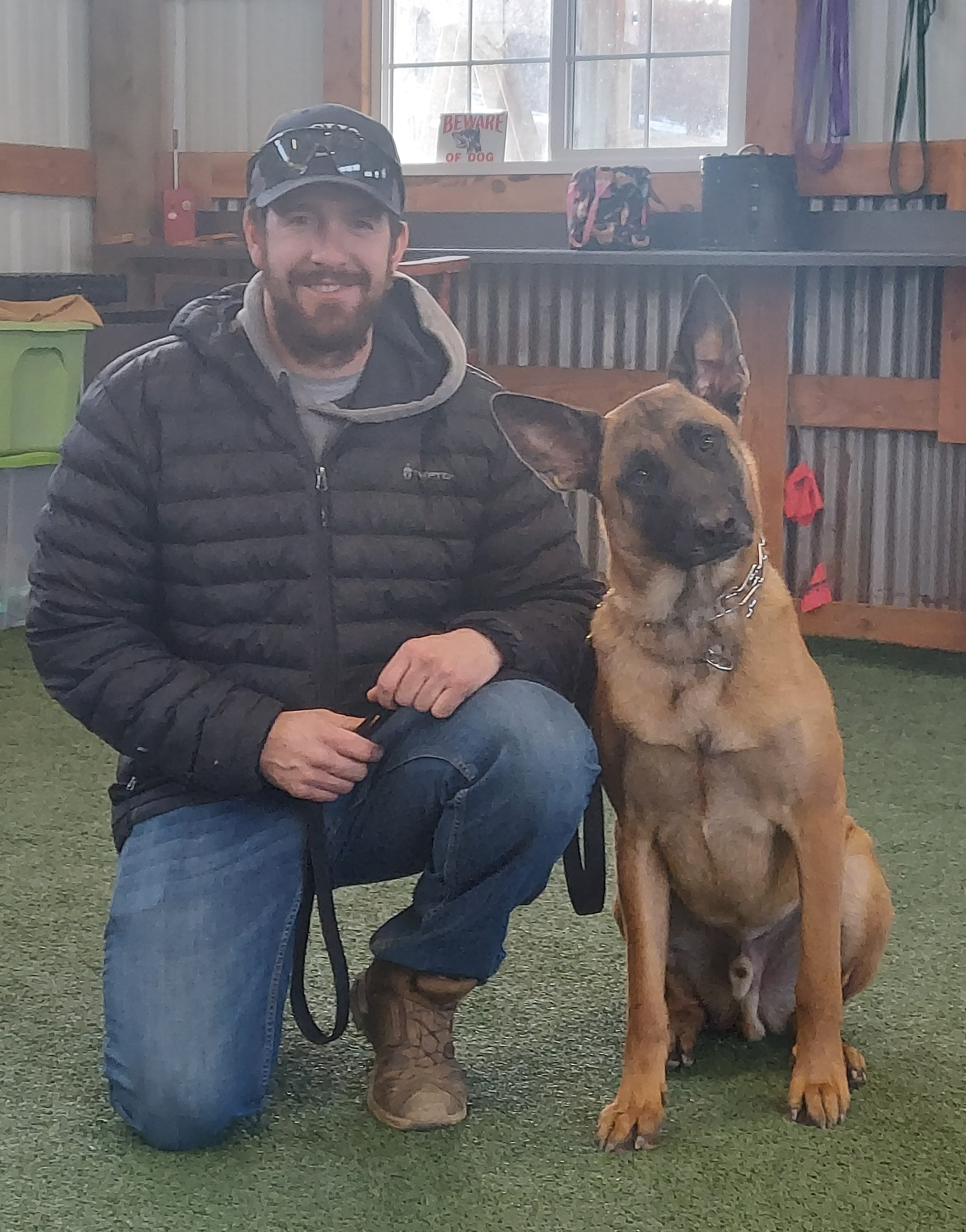 Owner kneeling with Belgian Malinois in training facility