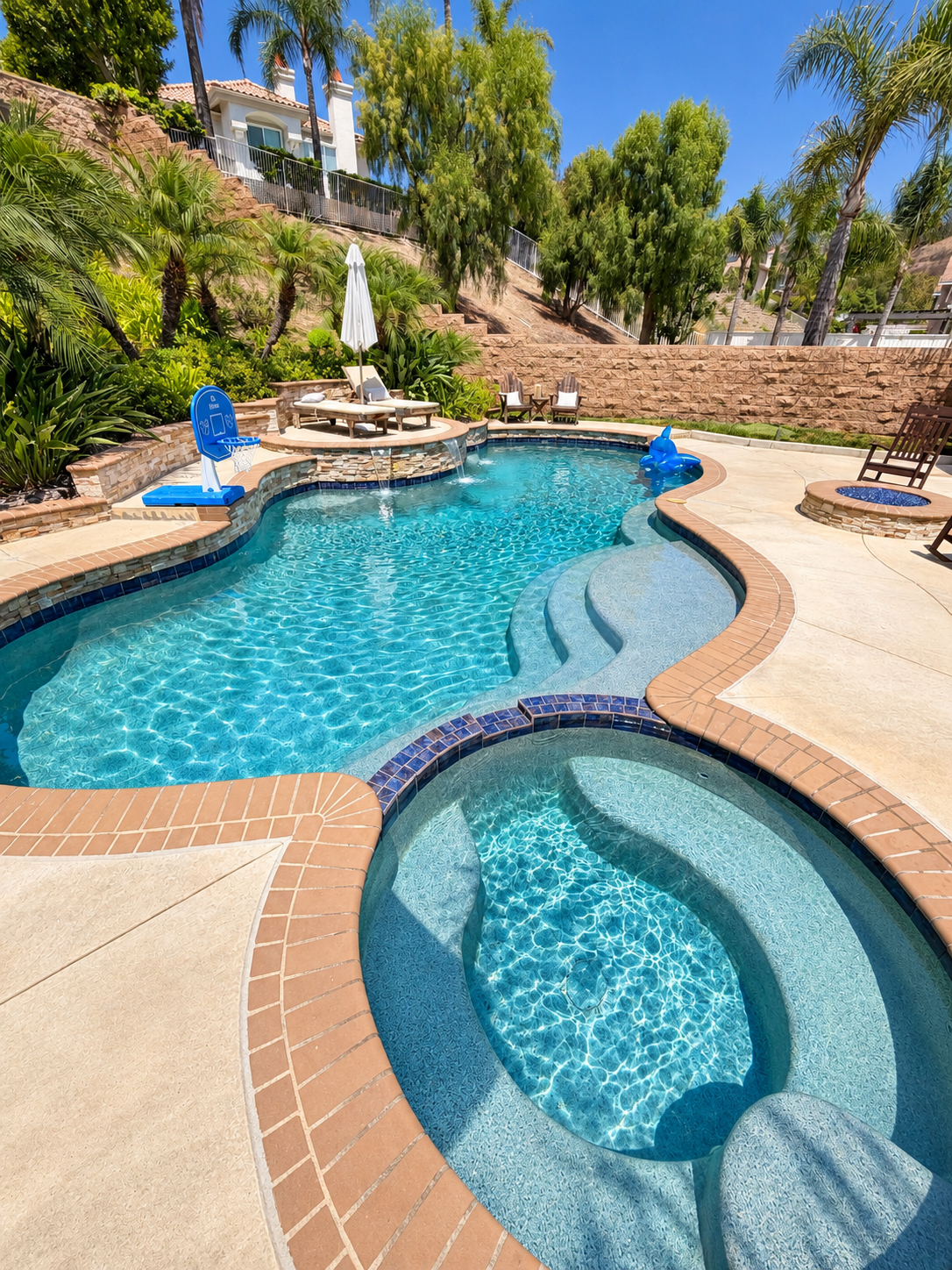 Custom residential swimming pool and spa with brick coping and clear blue water in a backyard setting