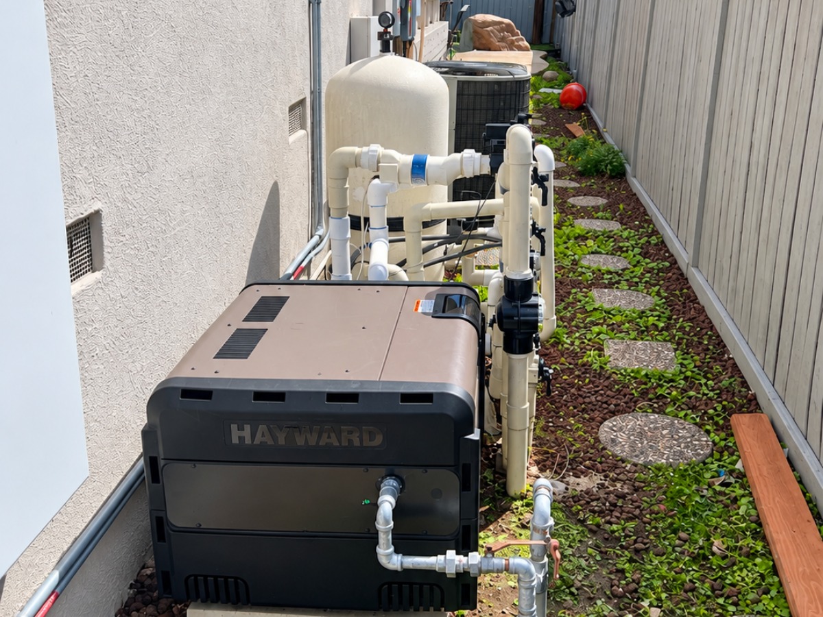 Hayward pool equipment pad with pool heater, filter tank, and plumbing installed along a residential walkway