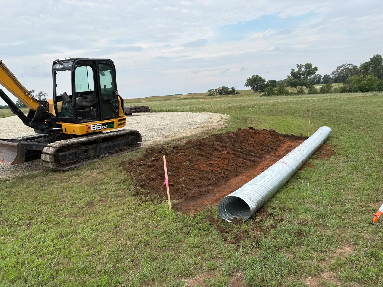 JCB excavator beside a corrugated metal culvert pipe and a freshly dug trench