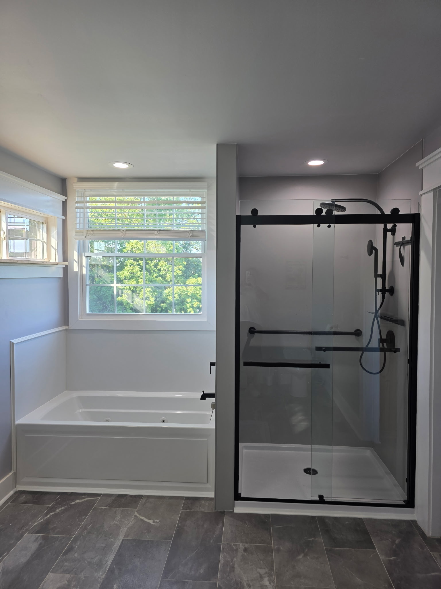 H&H Home & Bath Renovations completed luxury bathroom remodel featuring a modern soaking tub, sliding glass walk-in shower with matte black fixtures, and slate tile flooring
