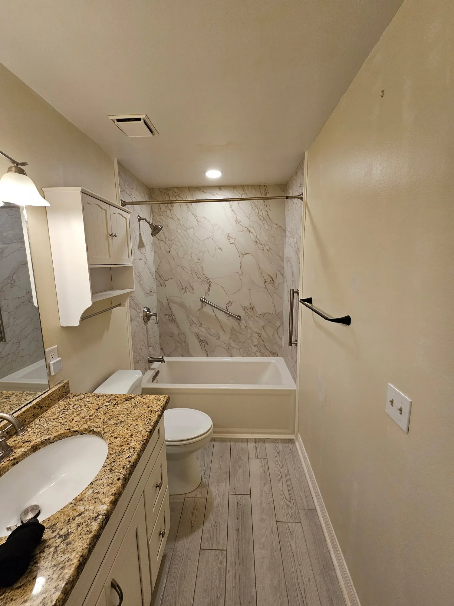 H&H Home & Bath Renovations completed full bathroom remodel with marble slab tub and shower surround, granite vanity, and wood-look plank tile floor