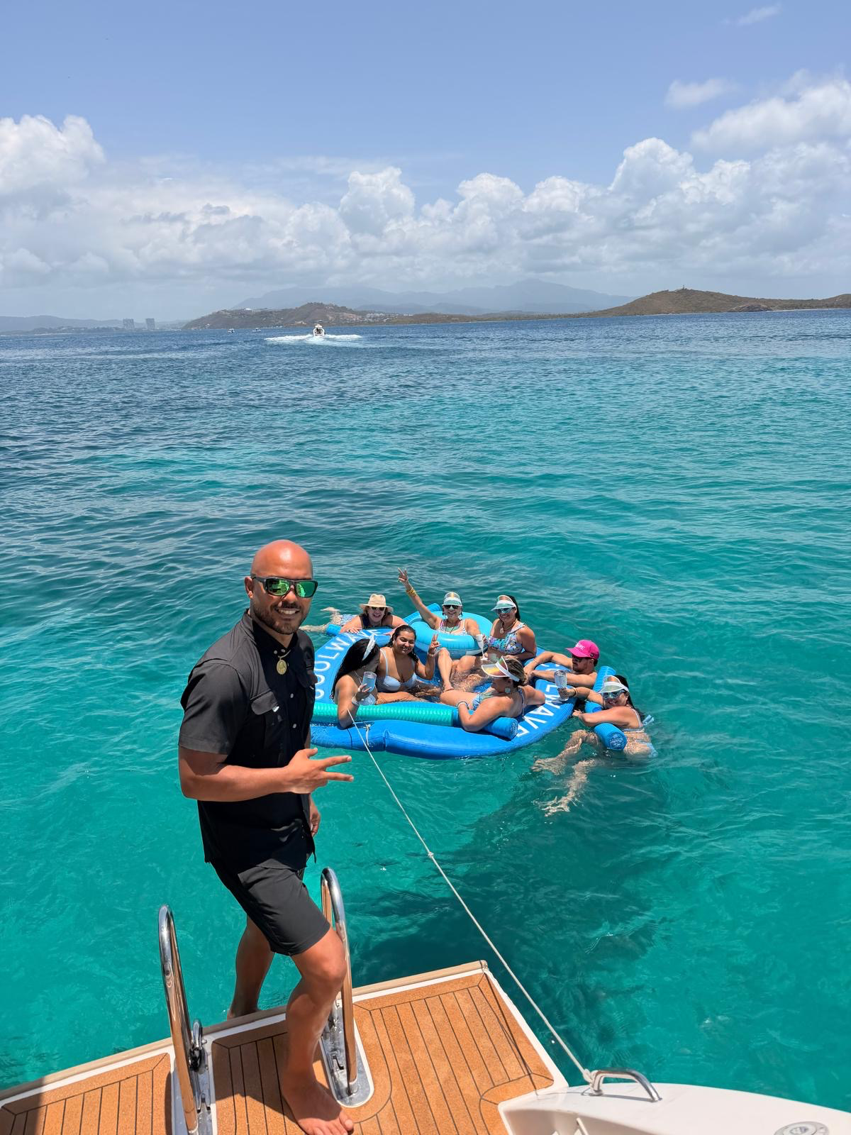 Guests on a large blue float in the water with crew member on ladder in foreground