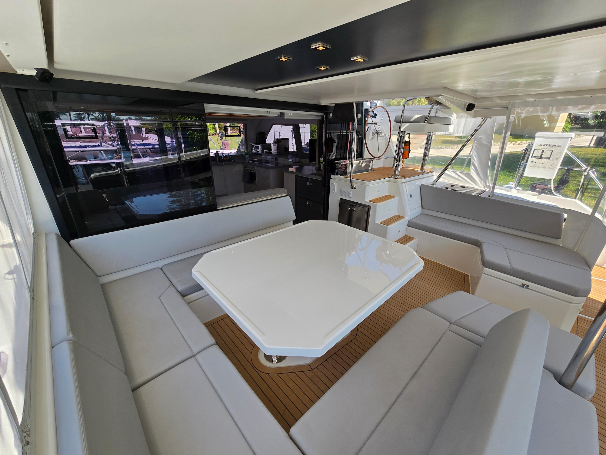 Covered aft dining area with gray upholstery, large glossy white table and teak-colored flooring