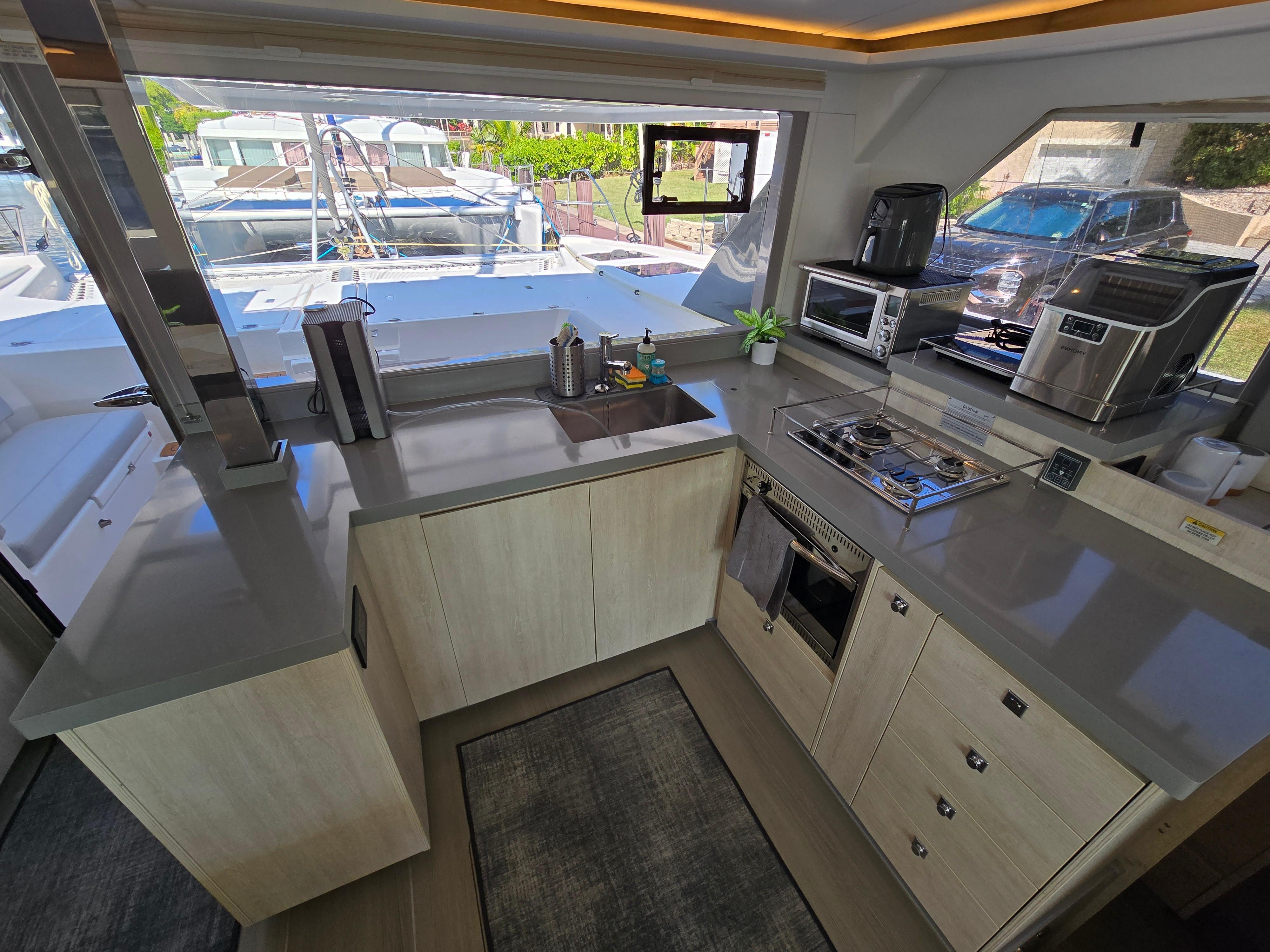 Interior galley with light cabinetry, gray counters, cooktop and appliances