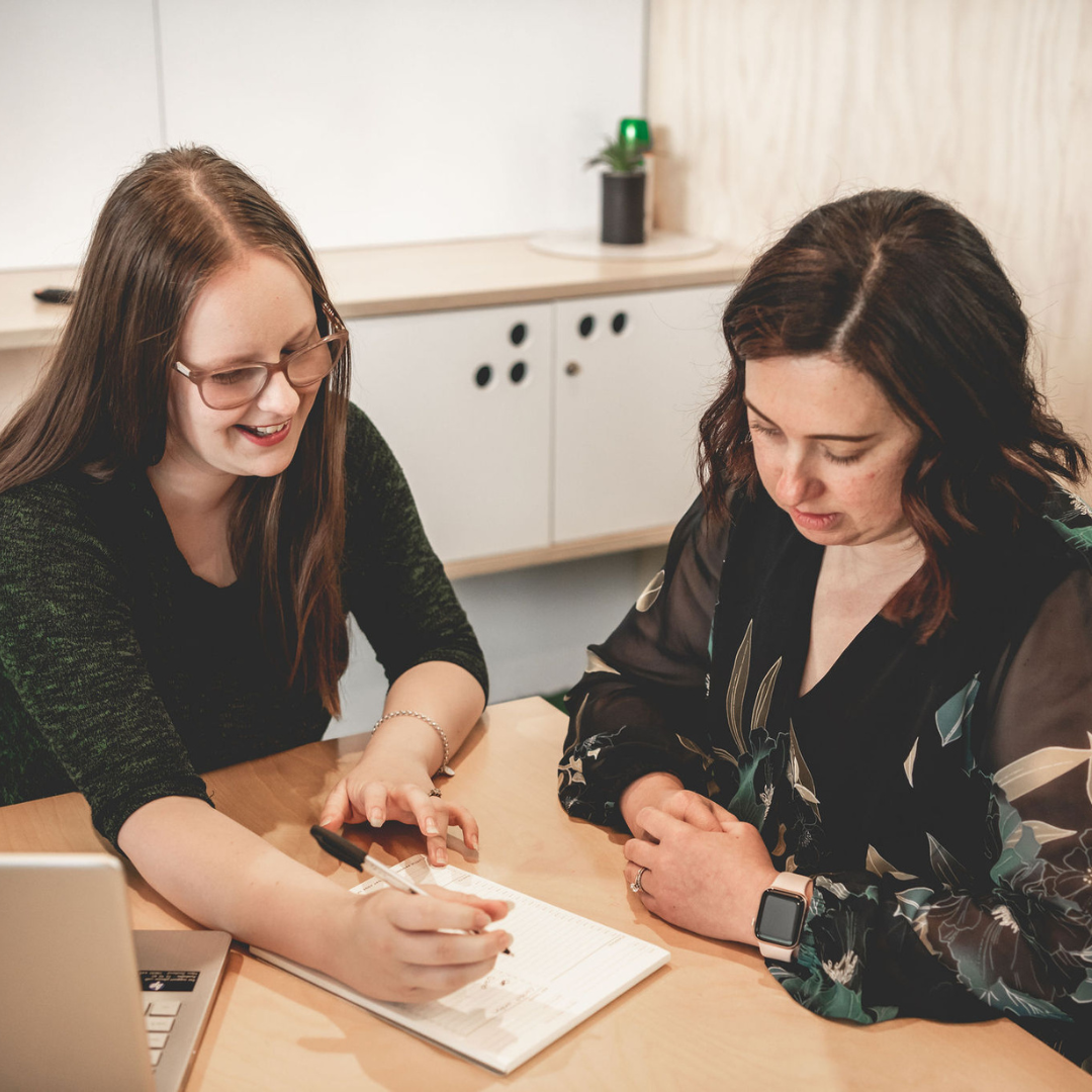 Caitlin collaborating with an allied health client over notes and a laptop