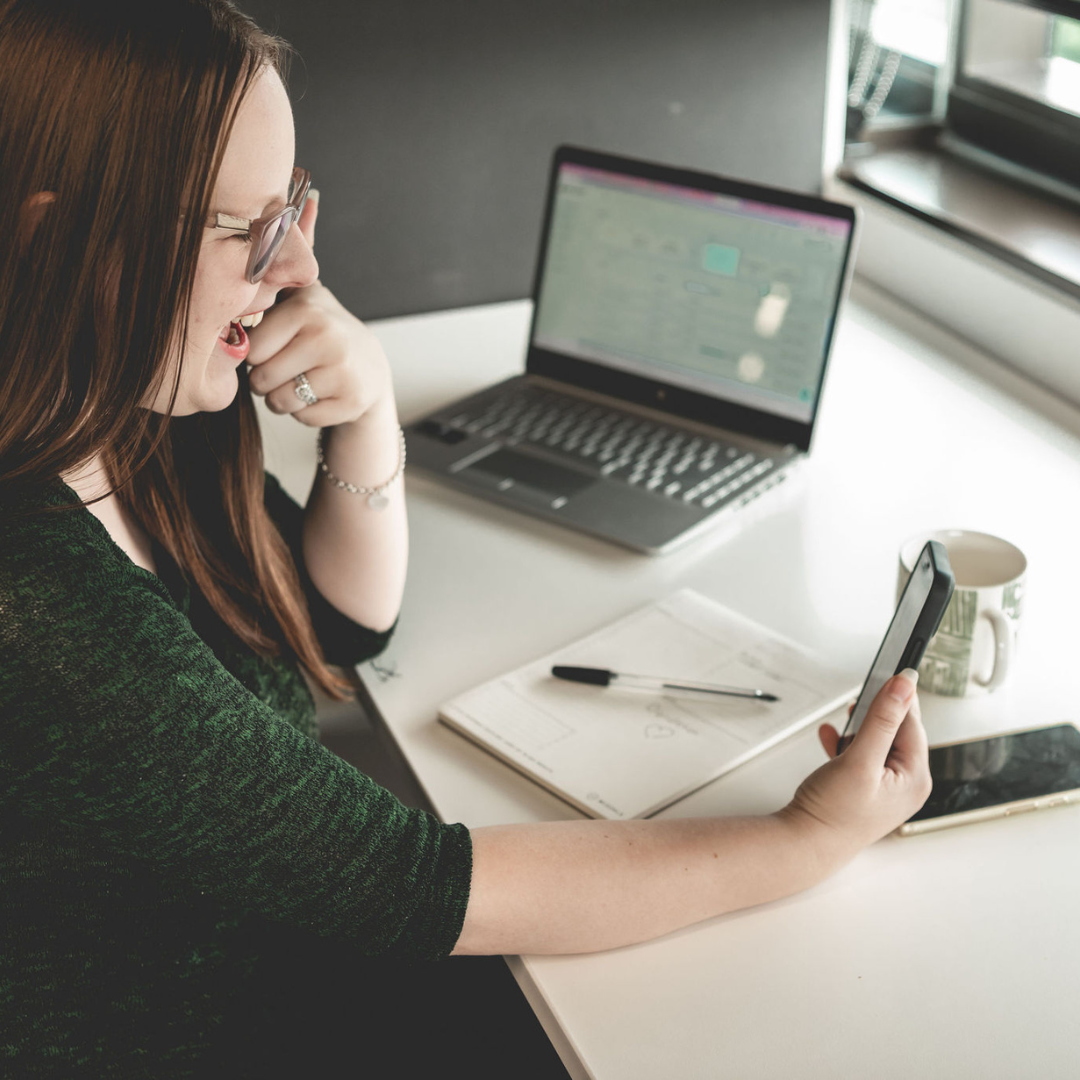 Caitlin celebrating client wins at her desk with phone and laptop