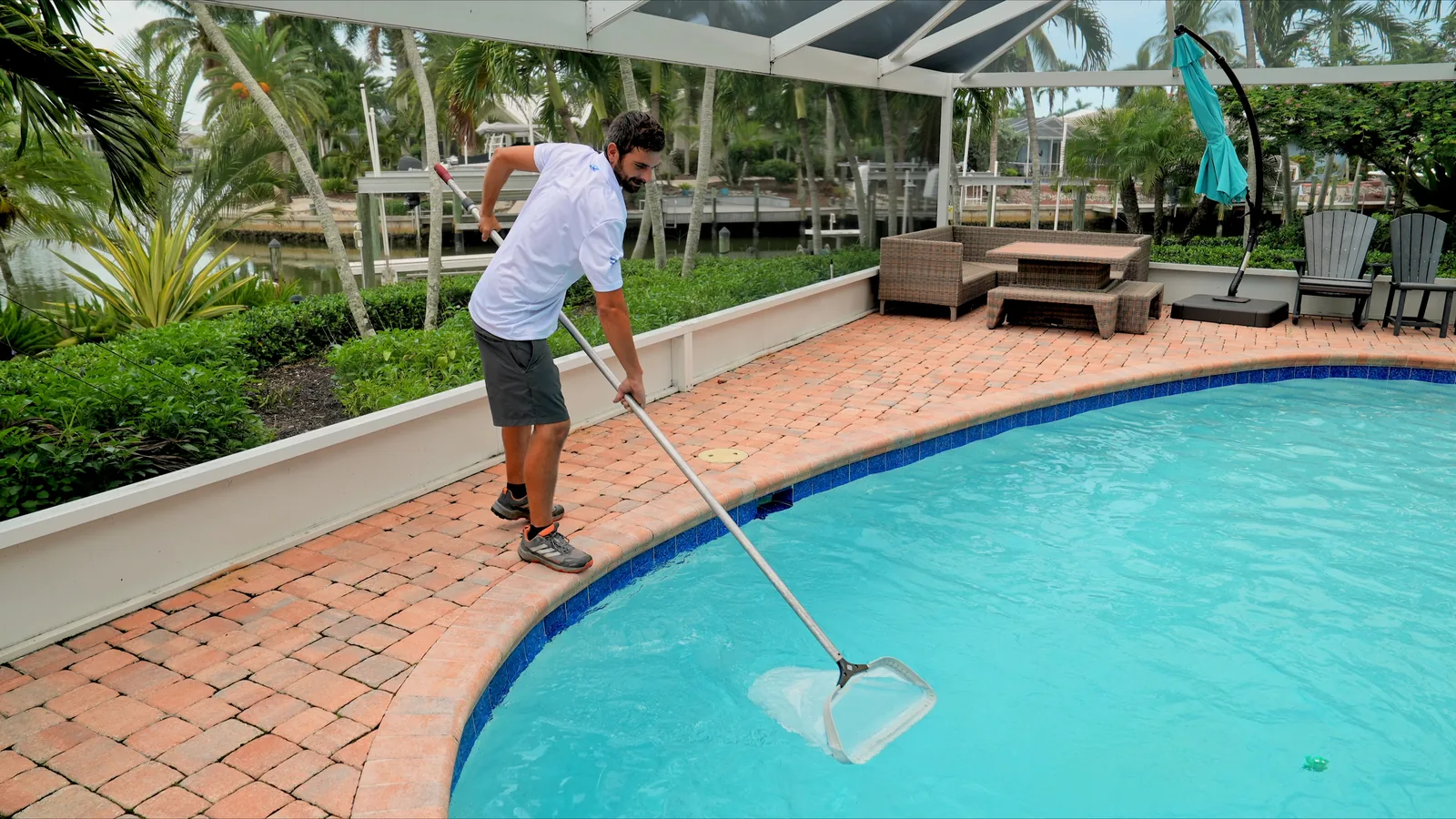 Pool technician skimming debris from a clean residential pool surface