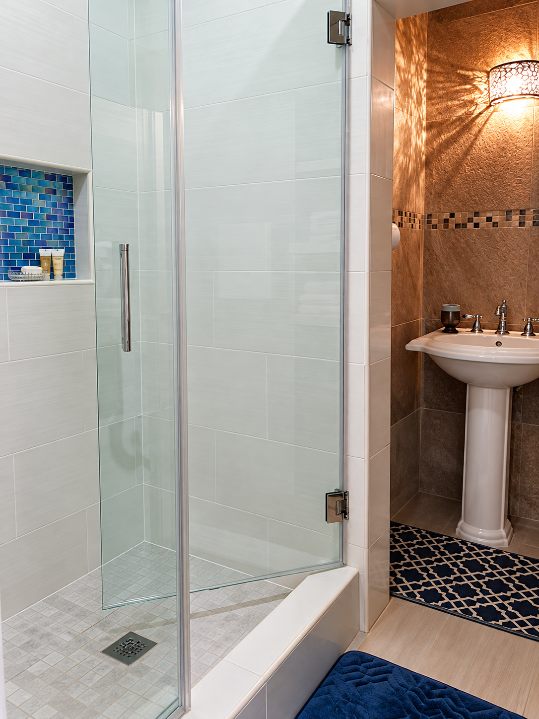 Modern glass-enclosed walk-in shower with blue mosaic tile niche and pedestal sink